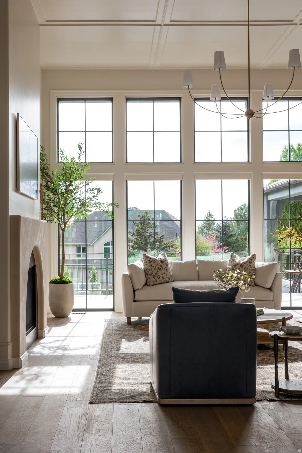 Double-height living space featuring expansive multi-pane windows, wood-finish flooring, a contemporary fireplace, and a coffered ceiling