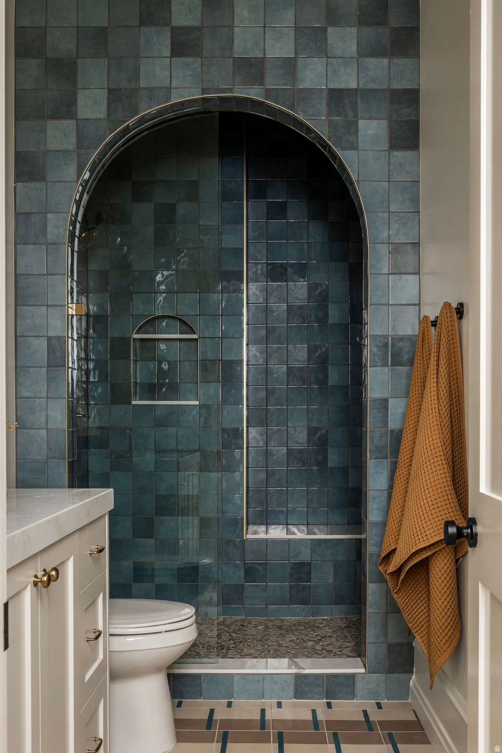 Arched shower enclosure with blue-toned square tiling, a built-in niche, and a stone-tiled floor
