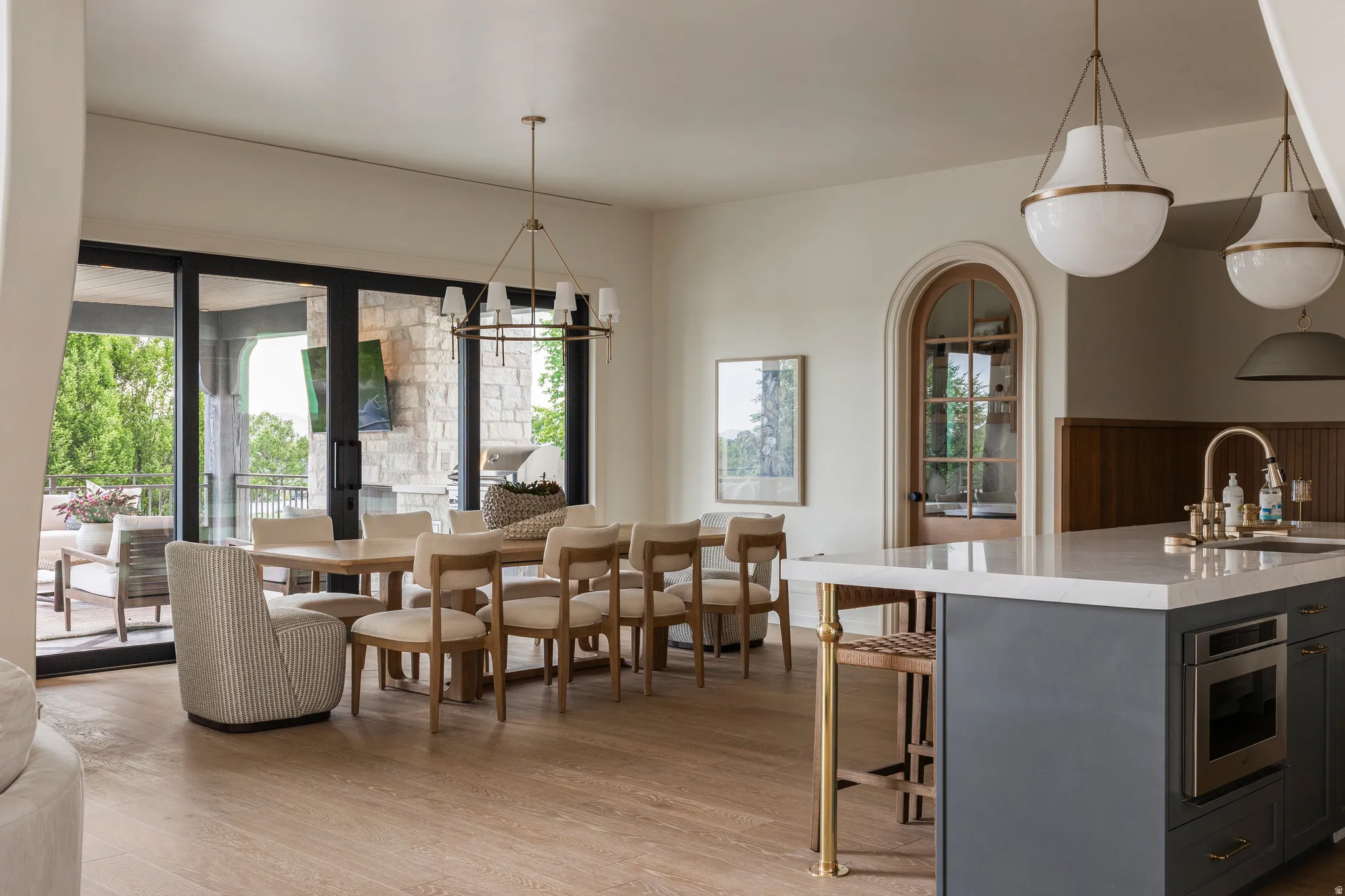 Spacious open-concept area featuring light wood-finish flooring, a contemporary kitchen island with a light-toned countertop, and two large pendant lights