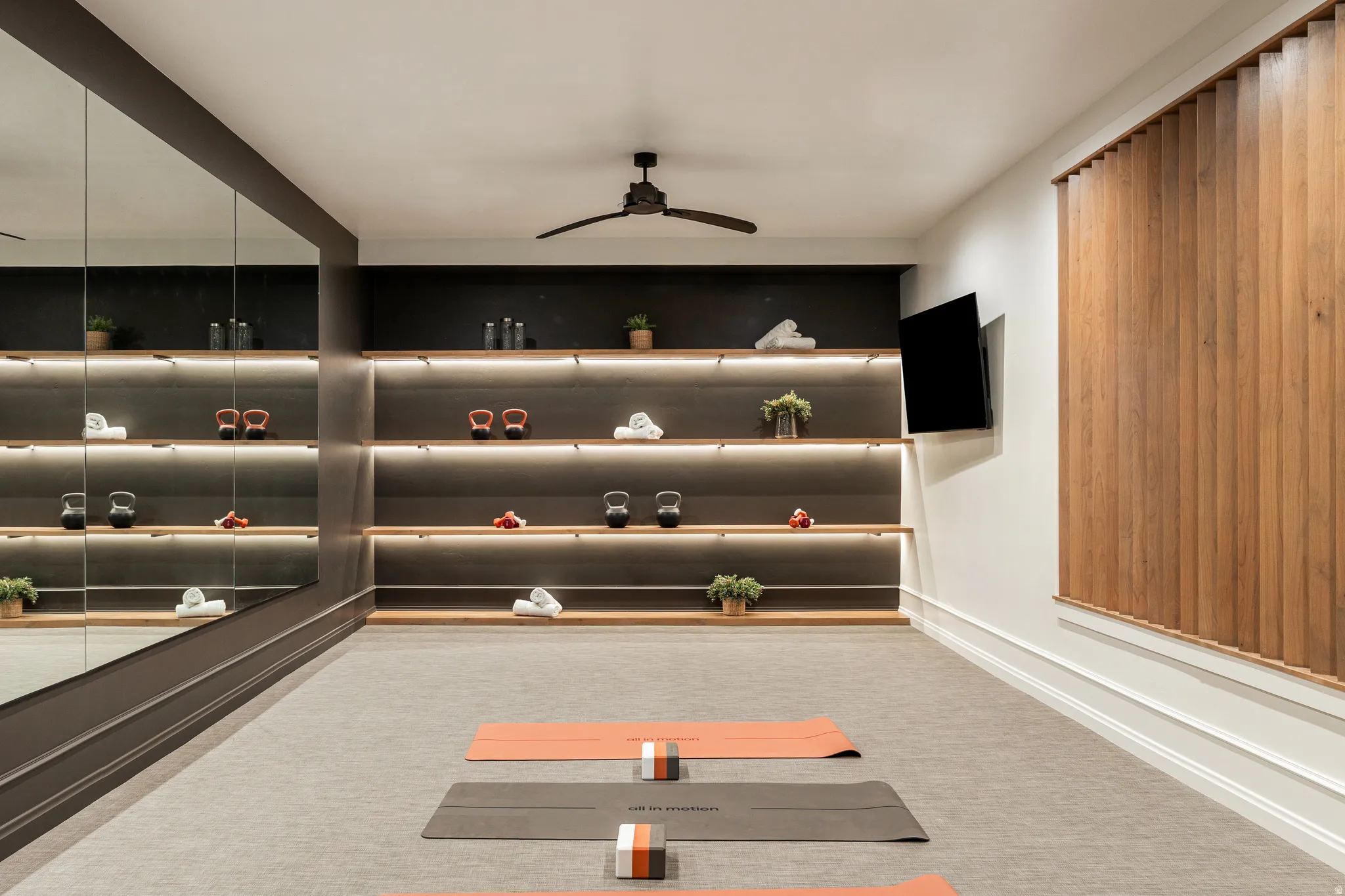 Dedicated fitness space featuring a full-wall mirror, integrated shelving with accent lighting, and a ceiling fan