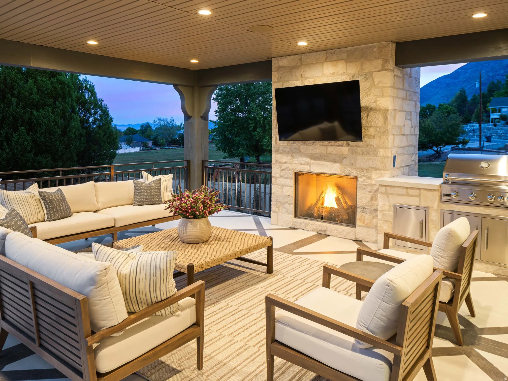 Covered outdoor patio featuring a stone fireplace, built-in outdoor grill, recessed lighting, and a mountain backdrop