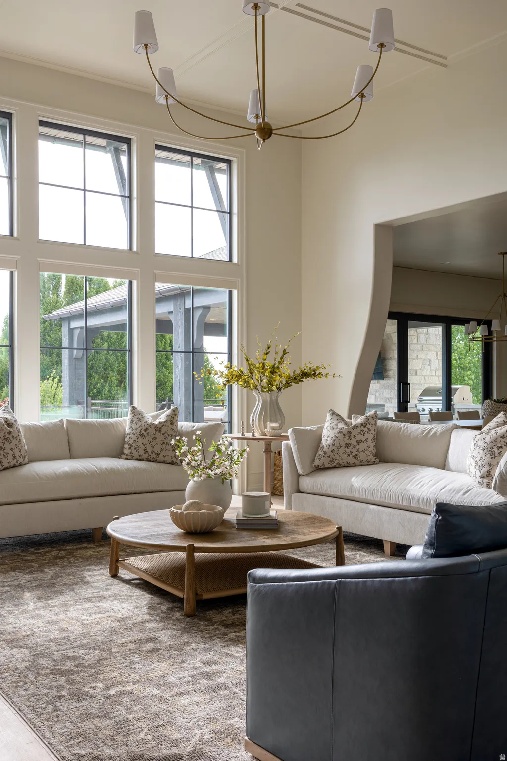 Grand living area featuring a high ceiling with exposed beams, tall windows with dark frames, and a contemporary chandelier
