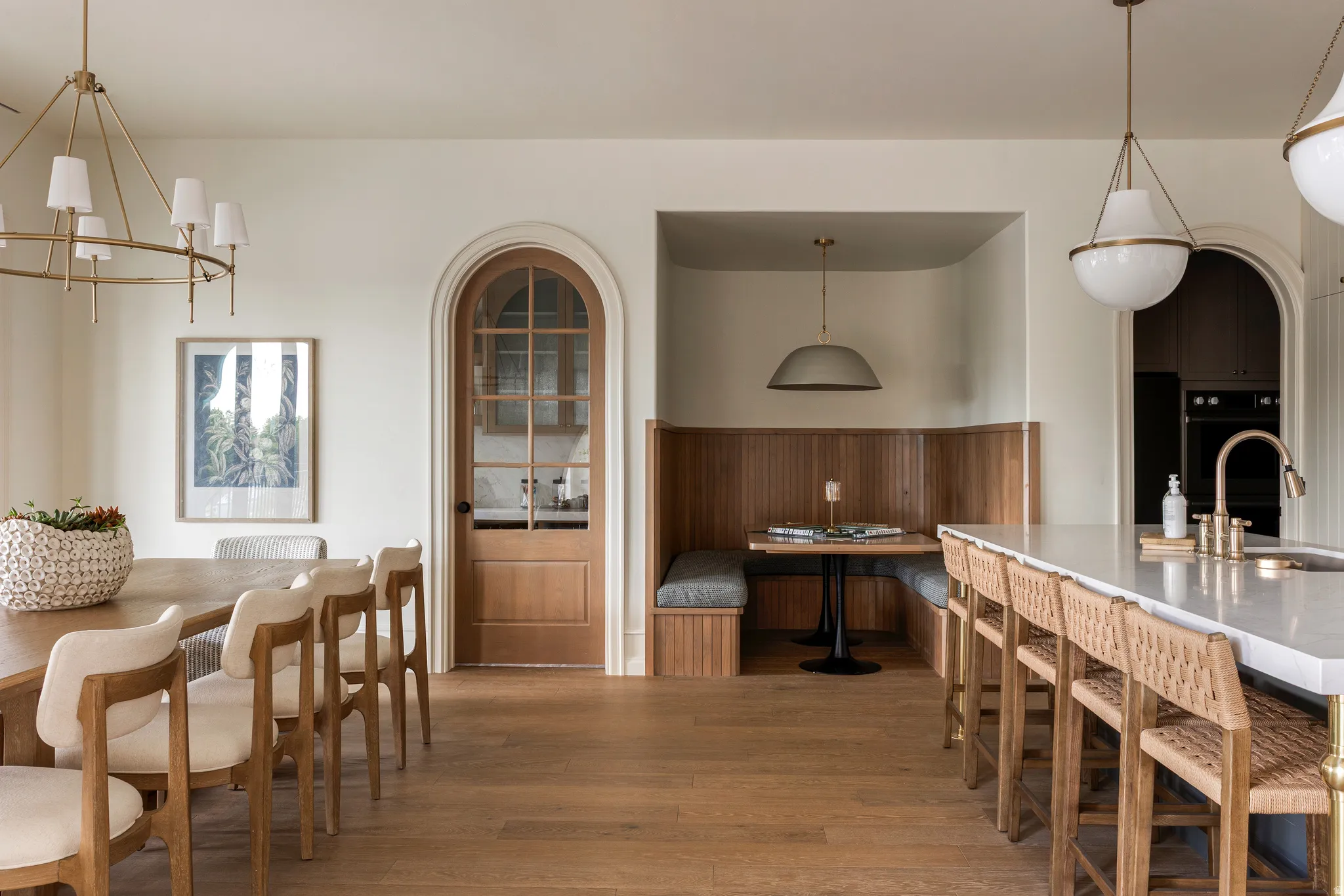 Open-concept space featuring wood-finish flooring, a built-in banquette, an expansive island with countertop seating, an arched doorway, and elegant overhead lighting fixtures