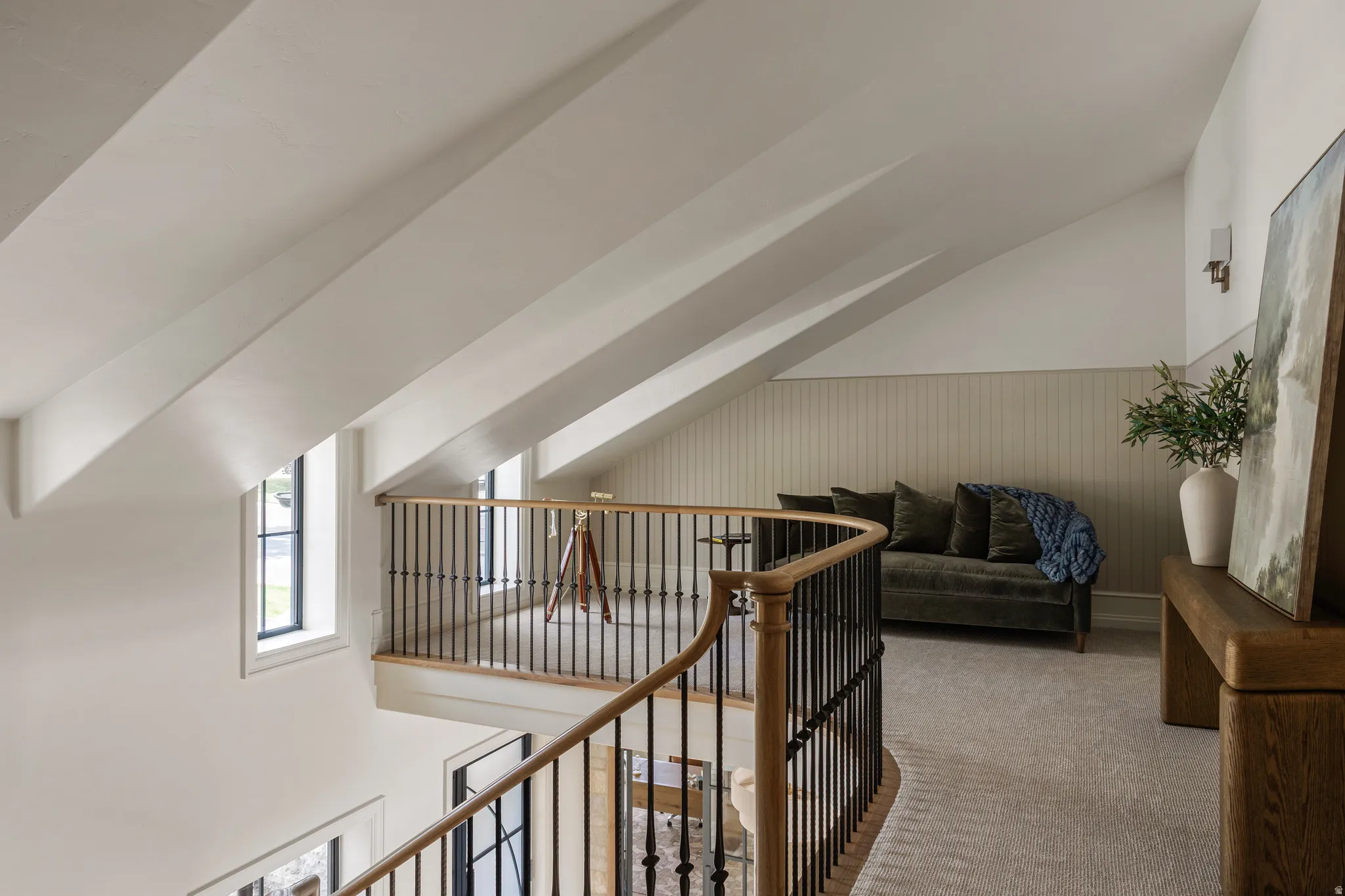Vaulted ceiling with exposed beams, open loft area, and hardwood handrail with wrought iron balusters