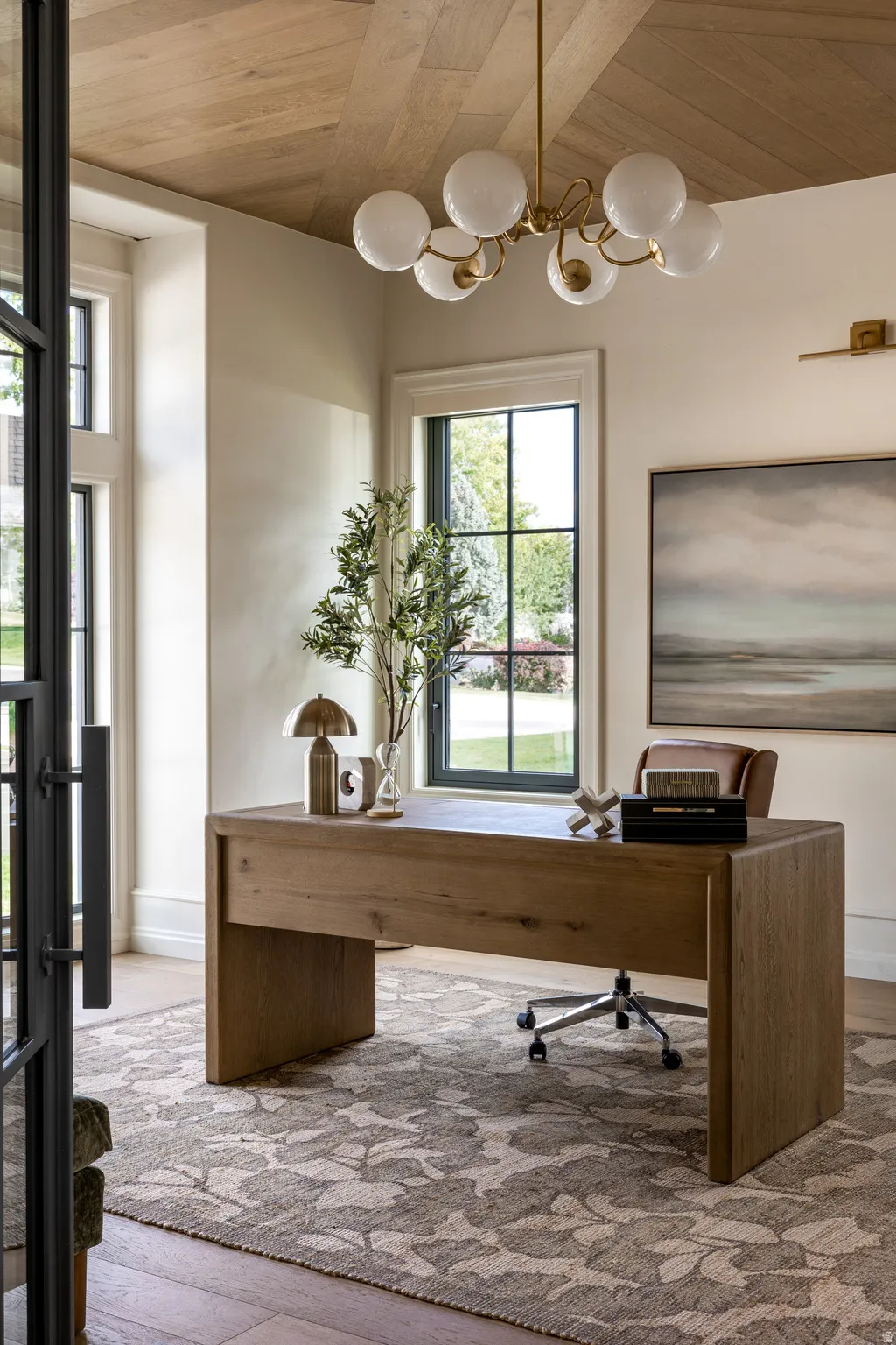 Hardwood herringbone ceiling with a contemporary chandelier, large windows with dark trim, and a built-in wood-finish desk
