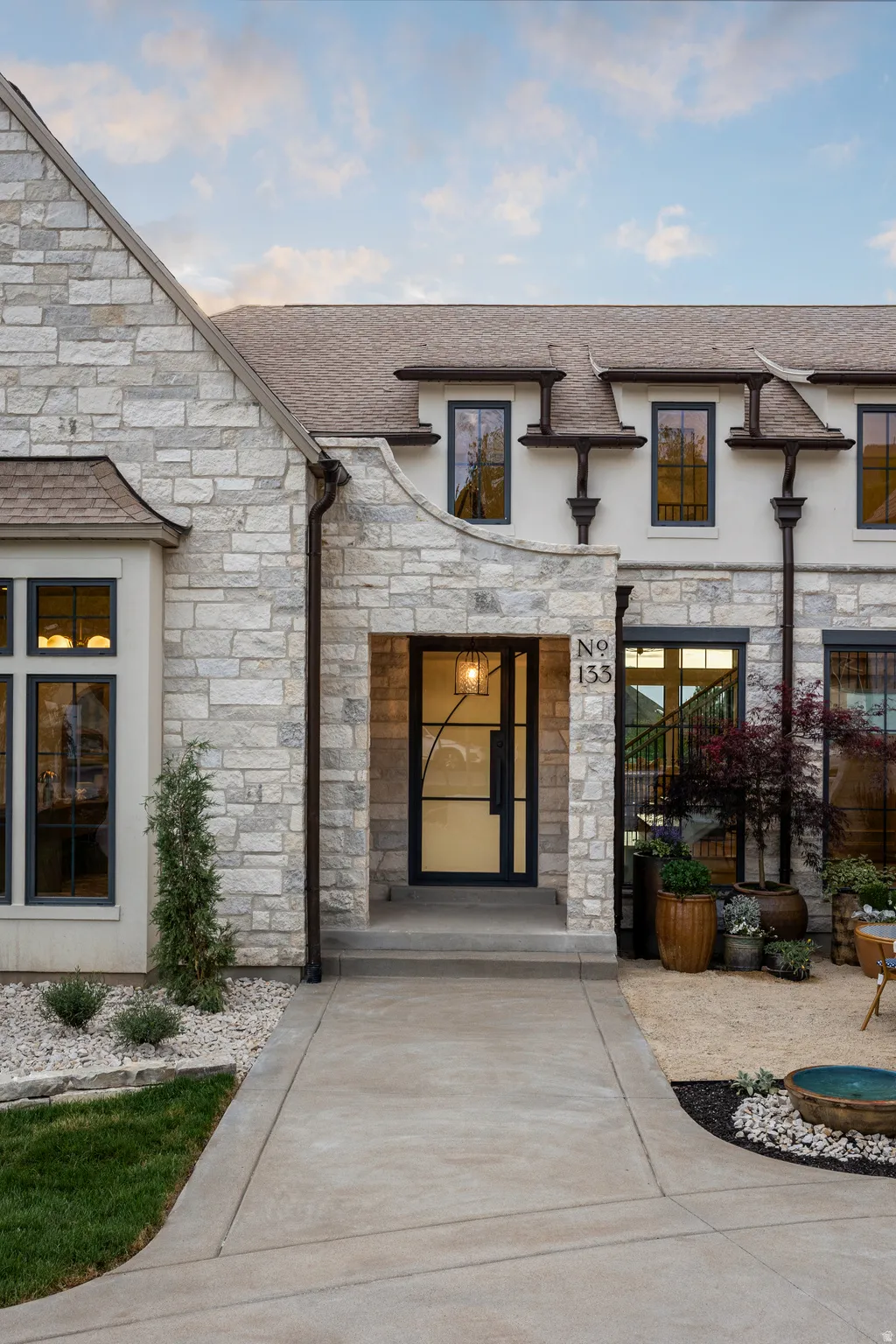 Stone facade with dark-framed windows, a prominent entry porch, and a modern glass-paneled front door