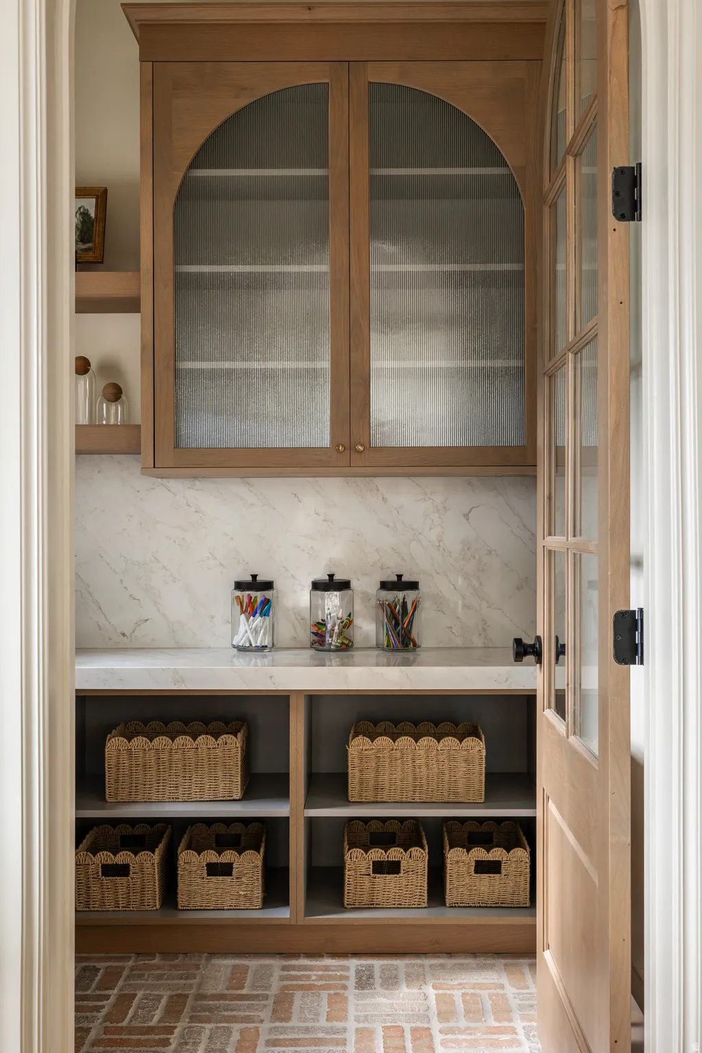Pantry featuring light wood cabinetry with arched glass doors, a stone countertop, and a matching stone backsplash