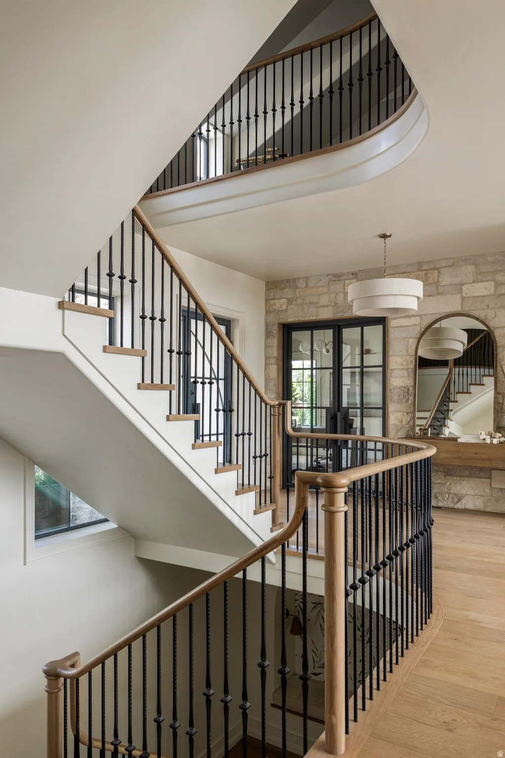 Grand curved staircase featuring natural wood handrails and wrought iron balusters