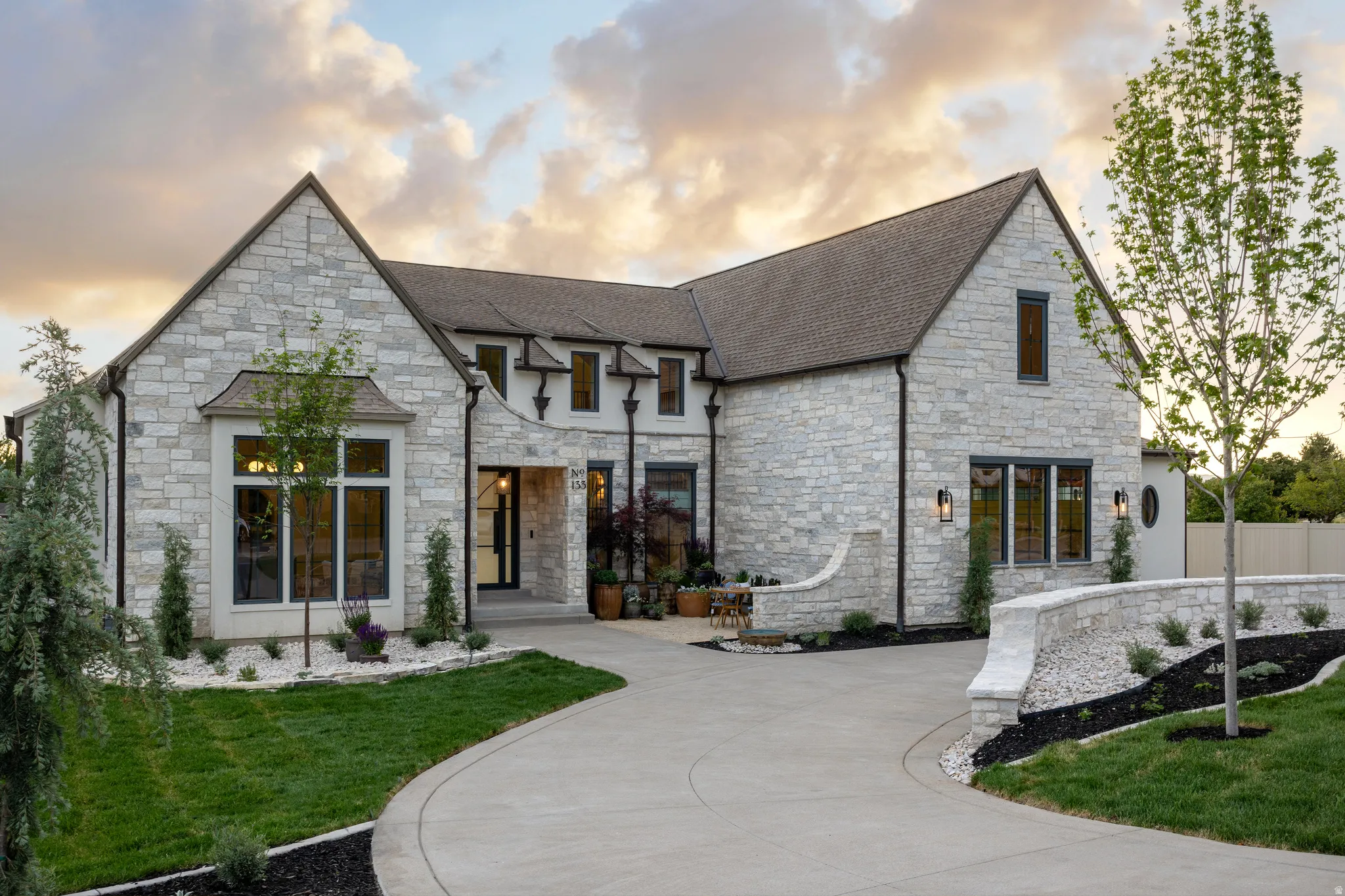 Stone facade residence featuring a prominent gabled roofline, custom driveway, and curated landscaping