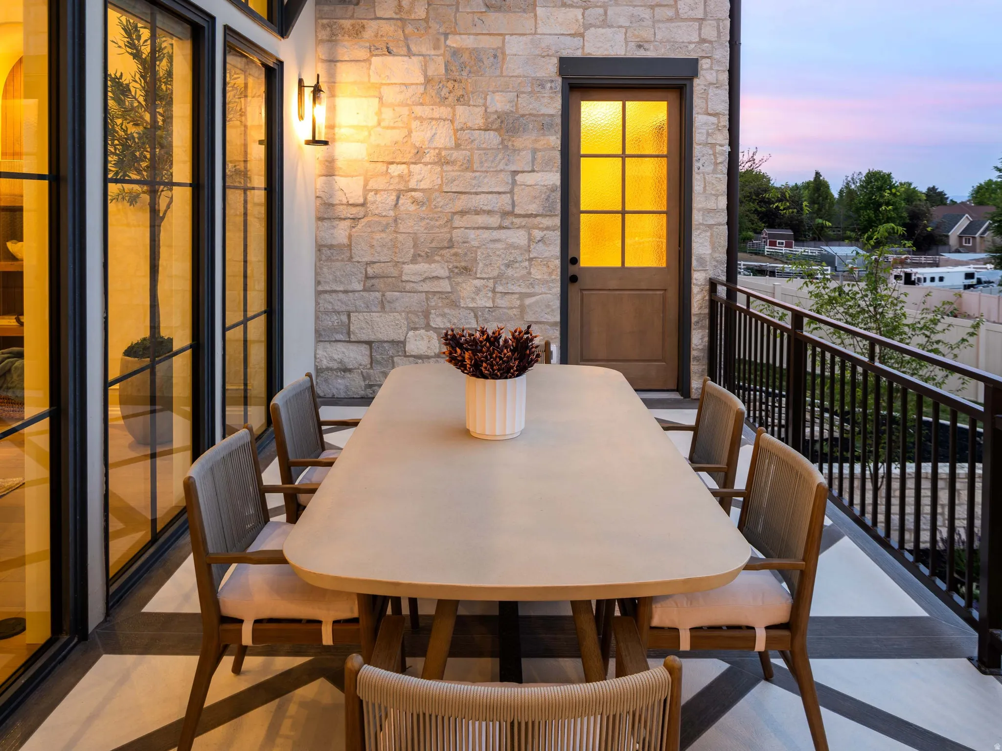 Spacious exterior balcony featuring stone veneer siding, black-framed glass panel doors, a solid wood door with glass inserts, and a black metal railing