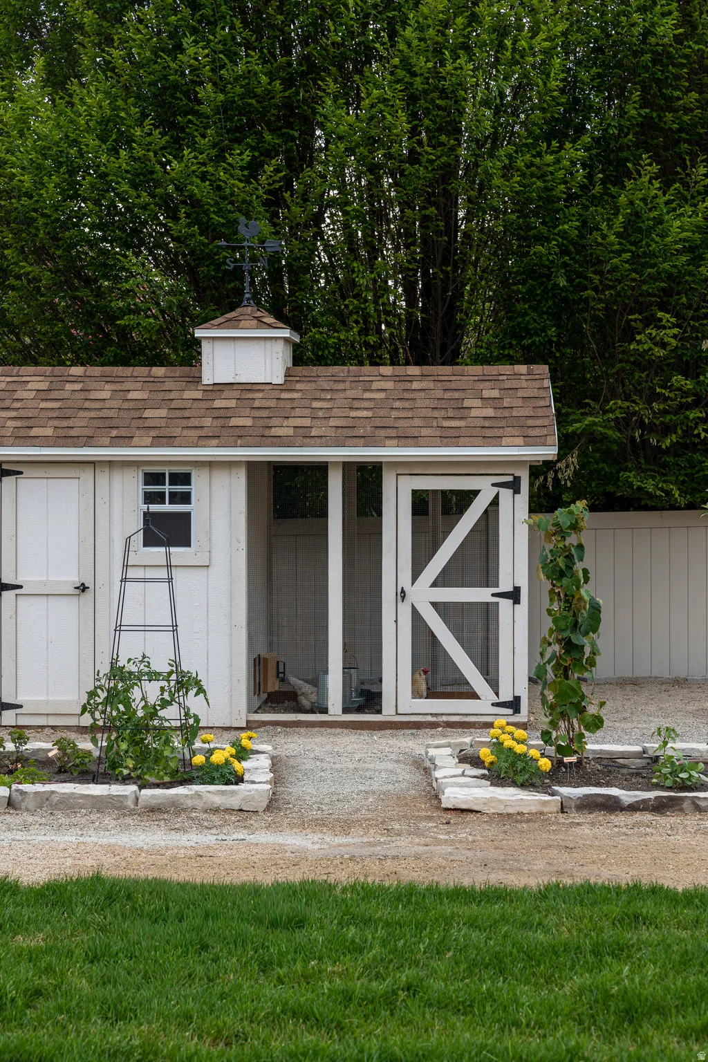 White outbuilding with a cupola and weathervane, featuring a brown shingle roof, barn-style doors, and a screened entry