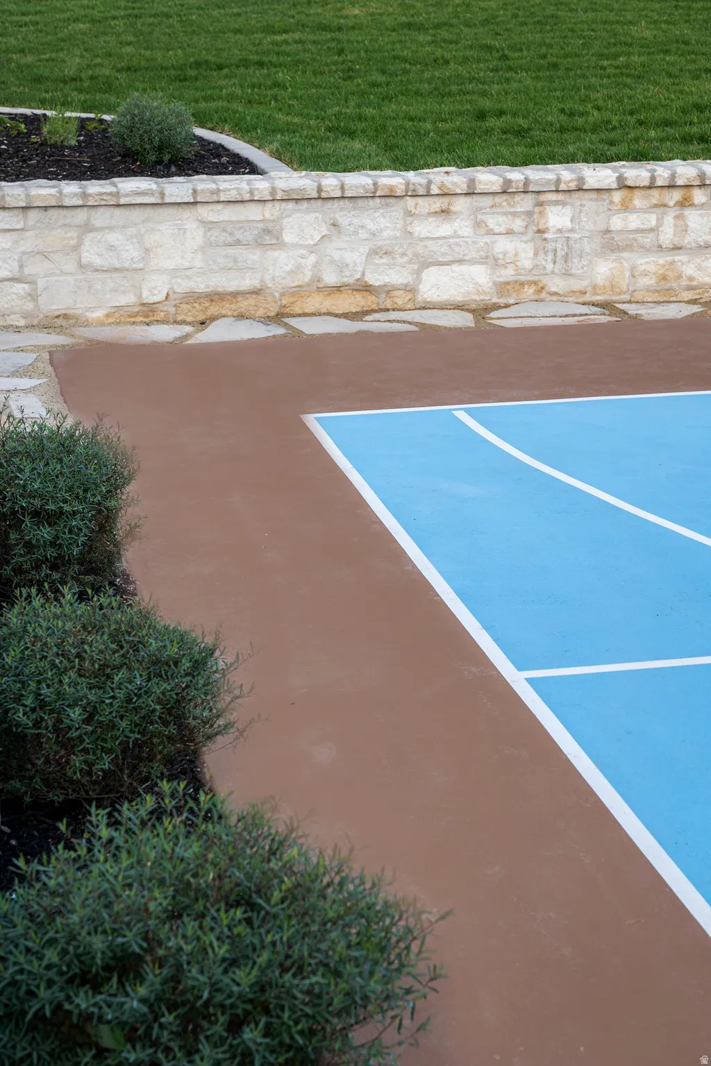 Recreational court with blue and white lines, bordered by a brown paved area