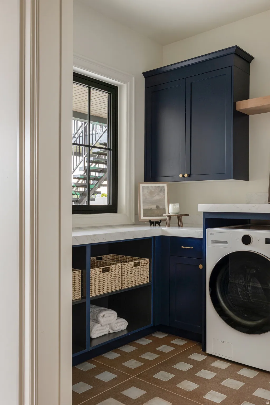 Laundry area featuring navy cabinetry, white countertops, checkerboard floor tiling, a single window, and a built-in appliance space
