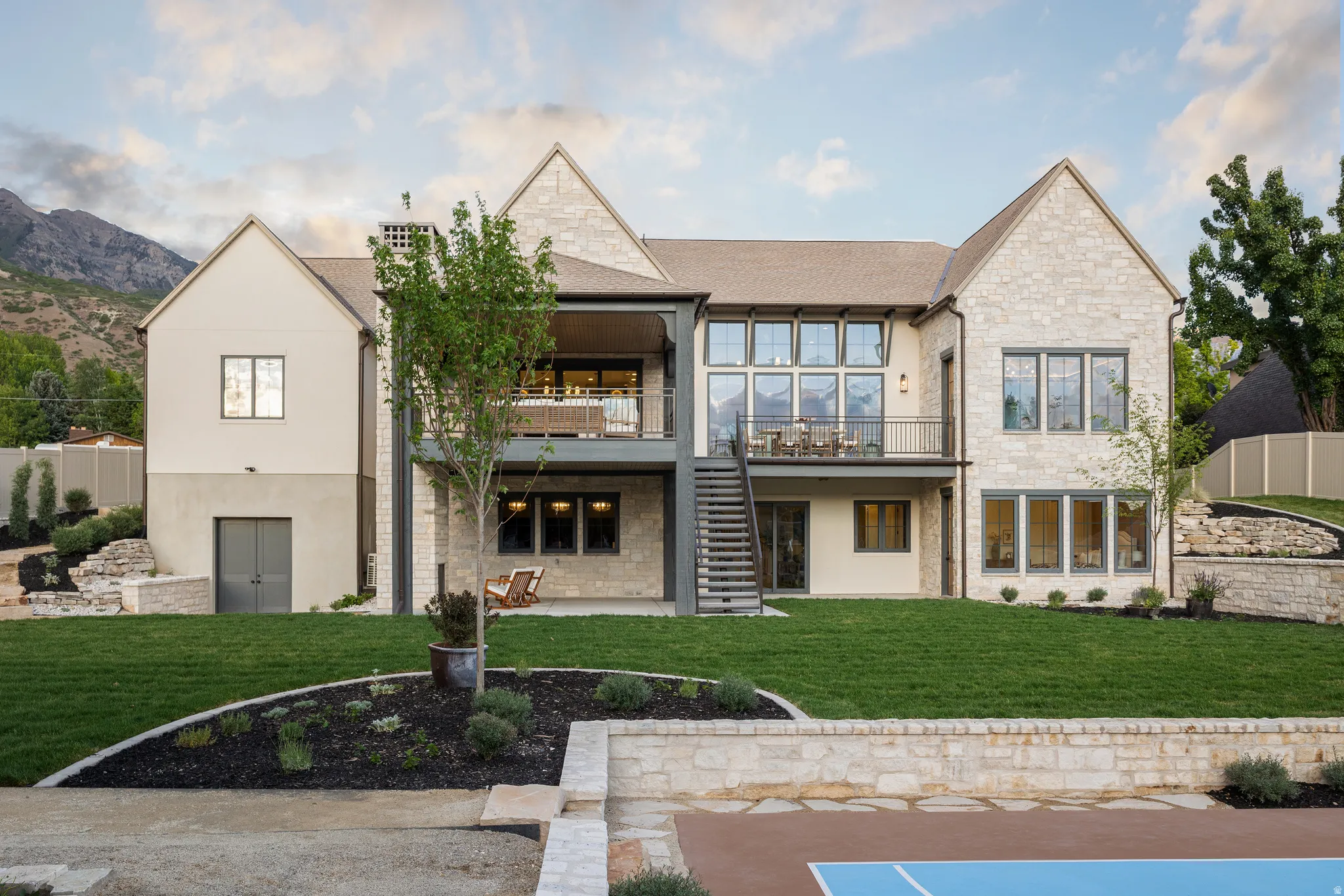 Expansive green lawn with tiered stone landscaping and a sport court