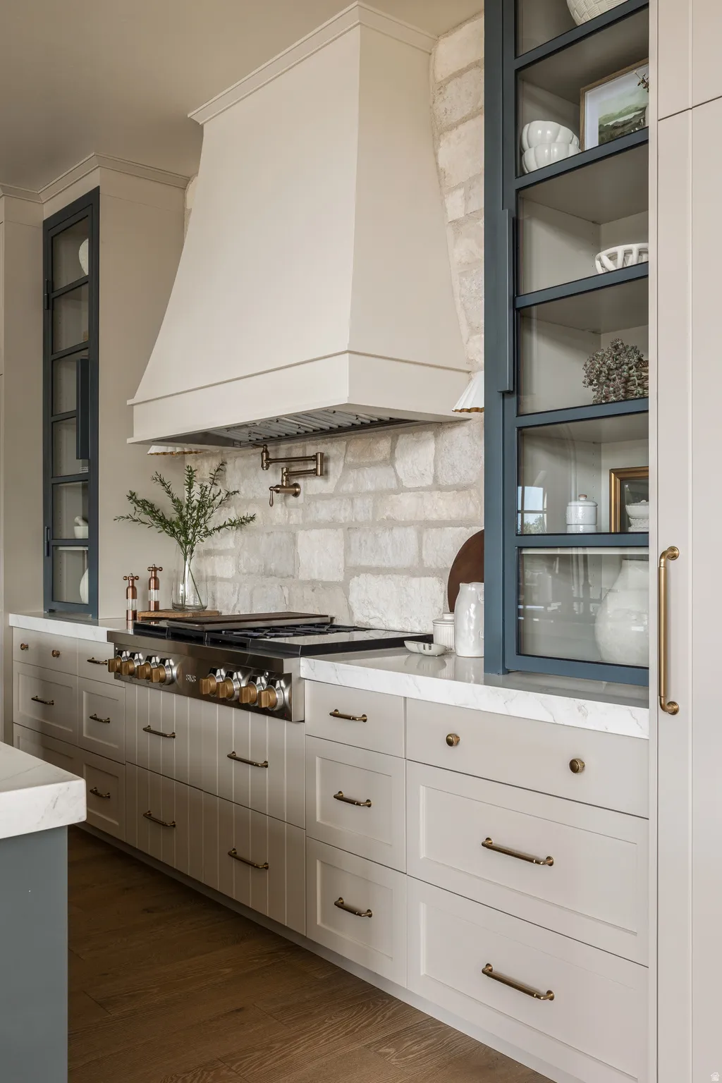 Gourmet kitchen featuring a stone accent wall, custom range hood, professional-grade range with a pot filler, extensive cabinetry with brass hardware, and a wood-finish flooring