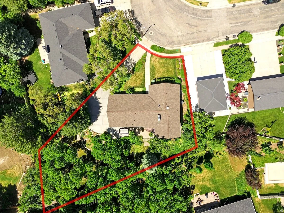 Single-story residence featuring a brown shingle roof, a generously sized lot, mature trees providing natural shading, a curved driveway, and ample green space