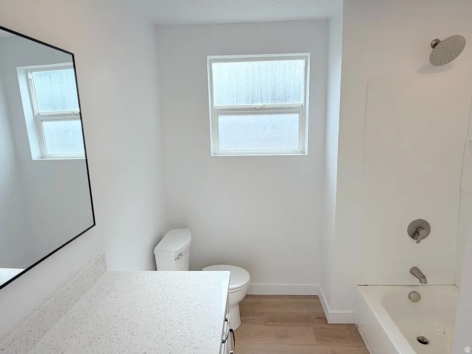 Bathroom featuring a quartz-finish countertop vanity with a black-framed mirror, a toilet, a window with frosted glass, and a tub-shower combination with brushed nickel fixtures