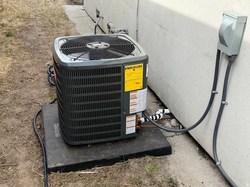 Exterior HVAC condenser unit featuring an EnergyGuide label, mounted on a durable pad, with electrical conduit and refrigerant lines connecting to the property