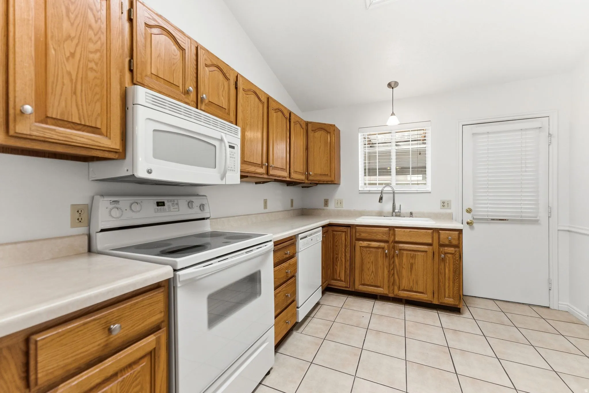Kitchen featuring light wood cabinetry with white knob hardware, white appliances, a double basin sink, and a window with horizontal blinds