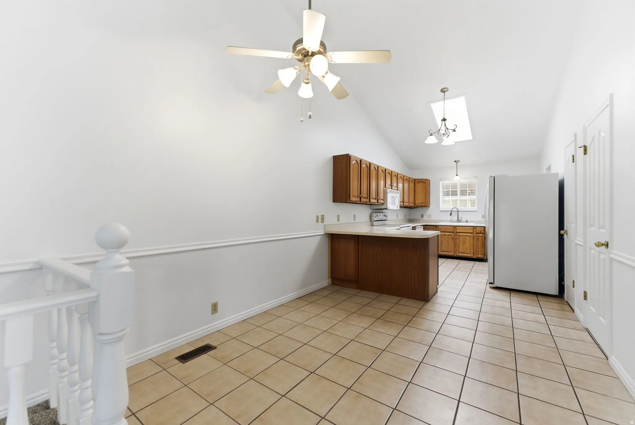 Kitchen area featuring a vaulted ceiling with skylight, tile flooring, and wood-finish cabinetry