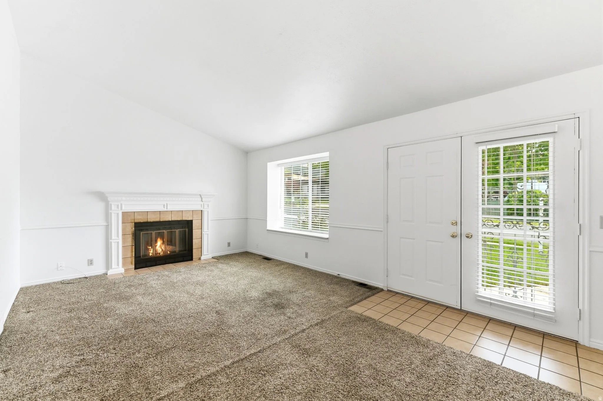 Living area featuring a fireplace with a white mantel and tile surround, a window with blinds, and a door with an accompanying sidelight