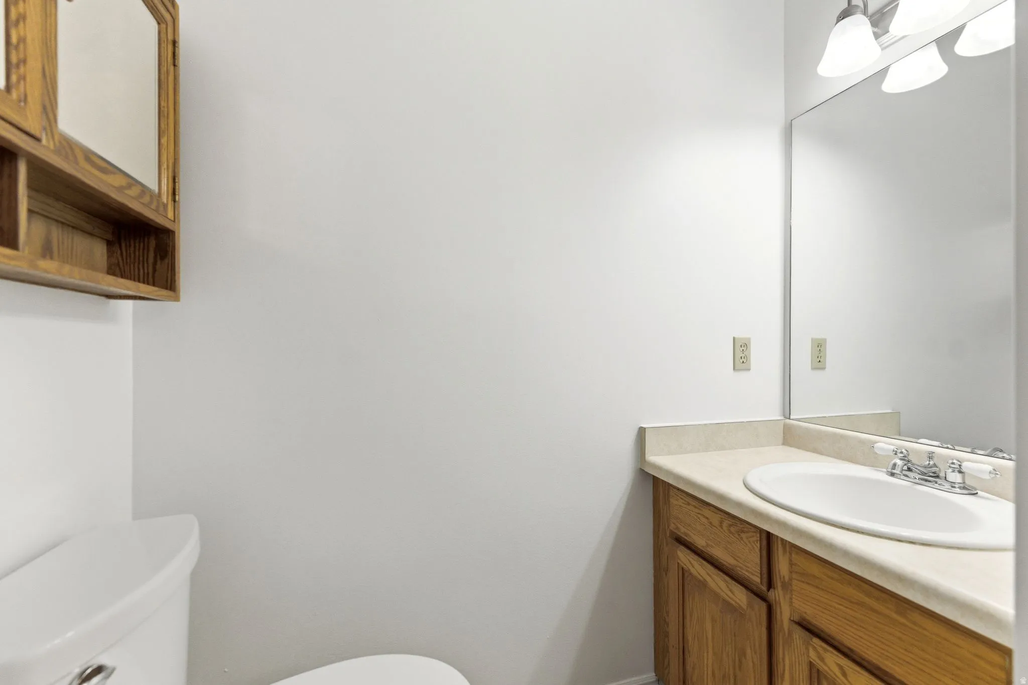Bathroom featuring a wood-finish vanity with an integrated sink, a large wall-mounted mirror, and a three-light vanity fixture