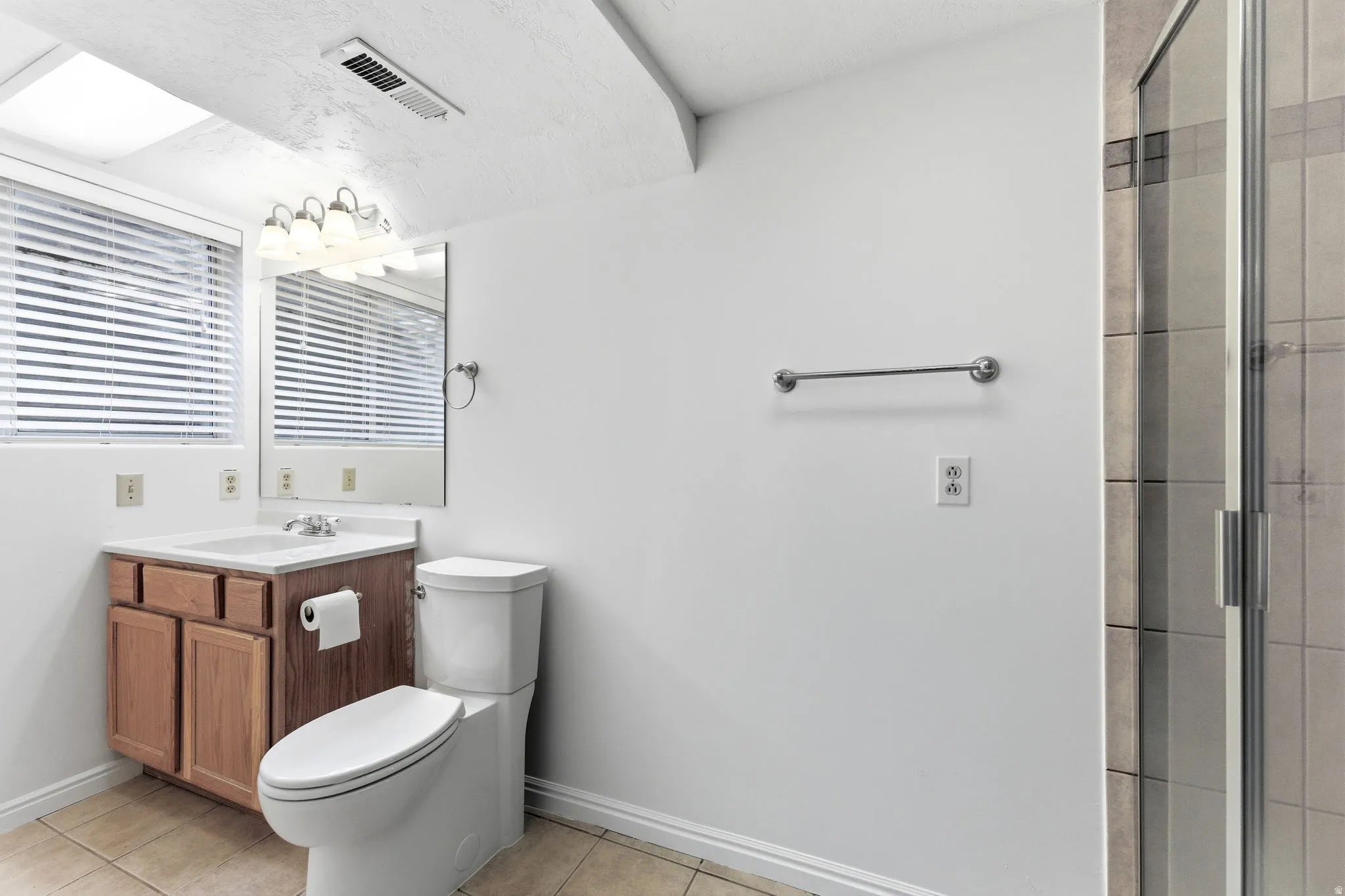 Bathroom featuring a wood vanity with a white countertop and integrated sink, a mirrored medicine cabinet, and a glass-enclosed shower with tiled walls