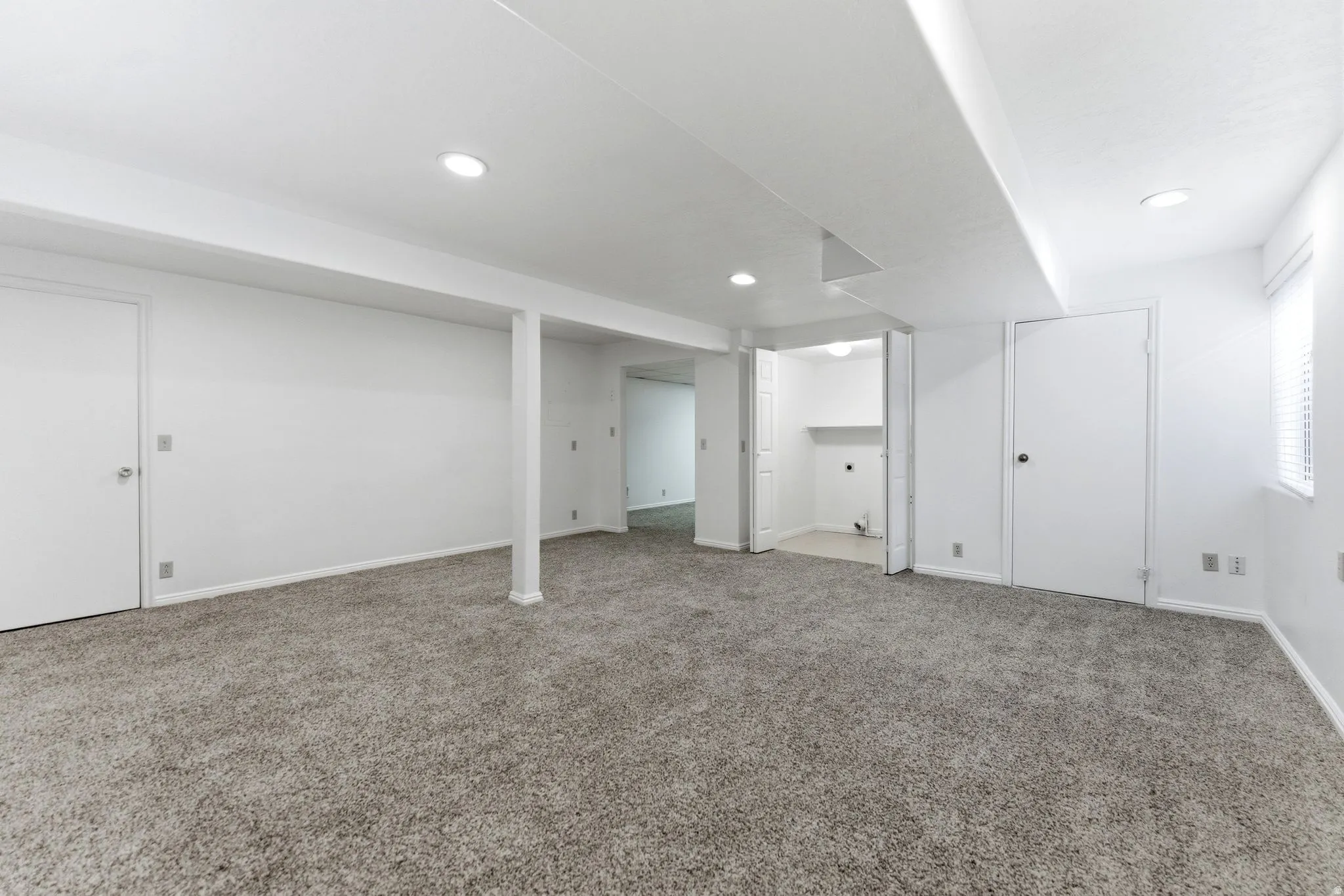 Expansive carpeted area featuring recessed lighting, a utility room with shelving, and a window with blinds