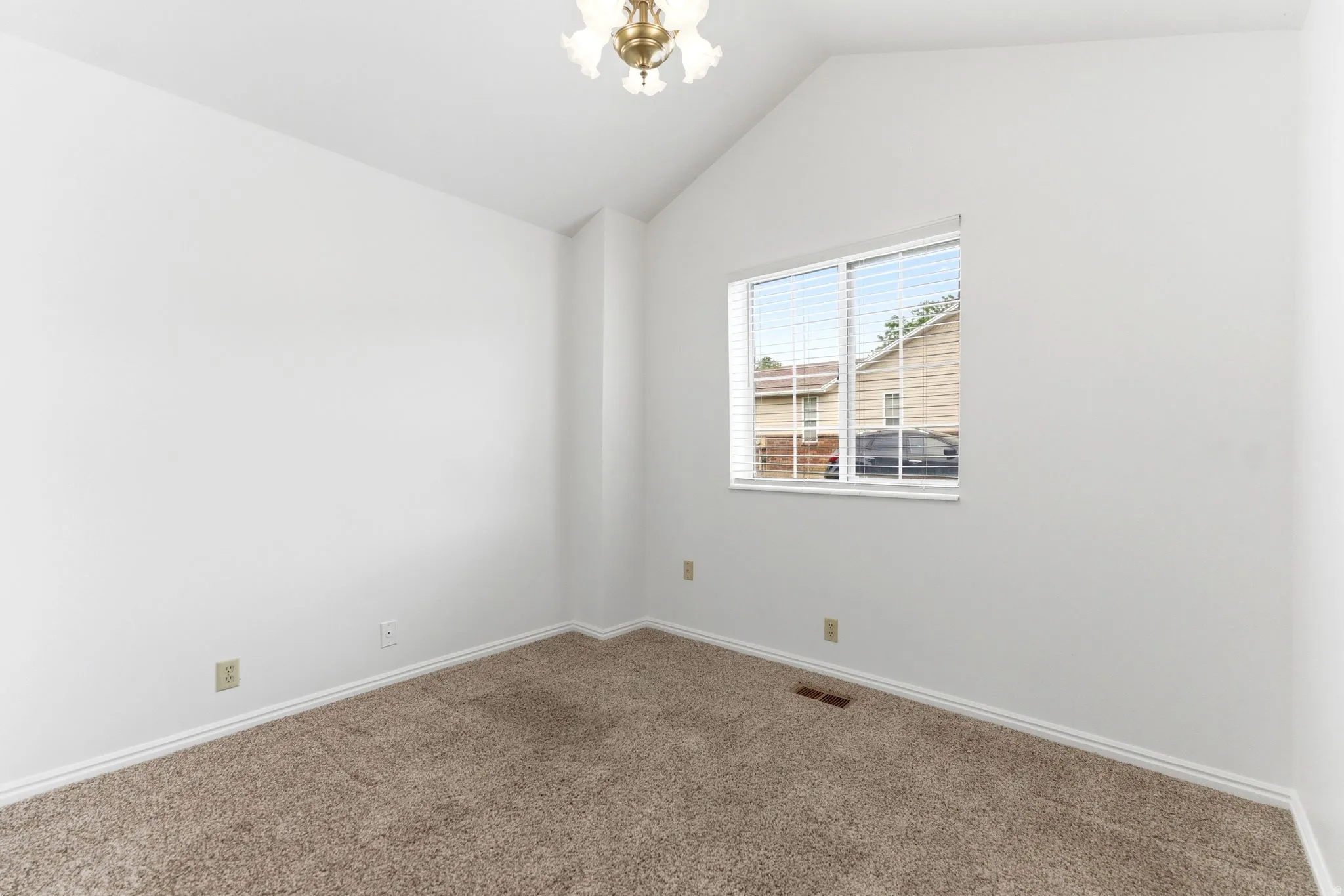 Vaulted ceiling room featuring light brown carpet, white baseboards, and a window with blinds