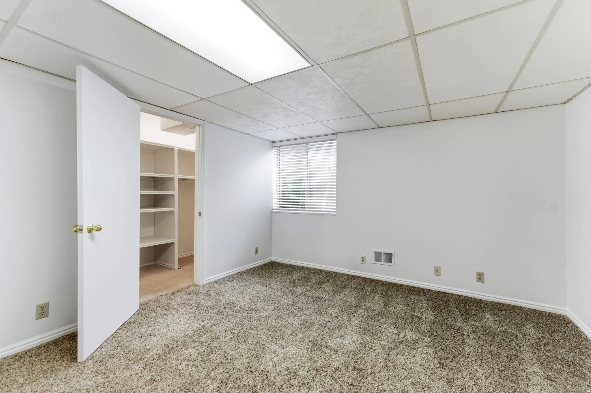 Spacious room featuring neutral carpeting, a window with blinds, and white walls