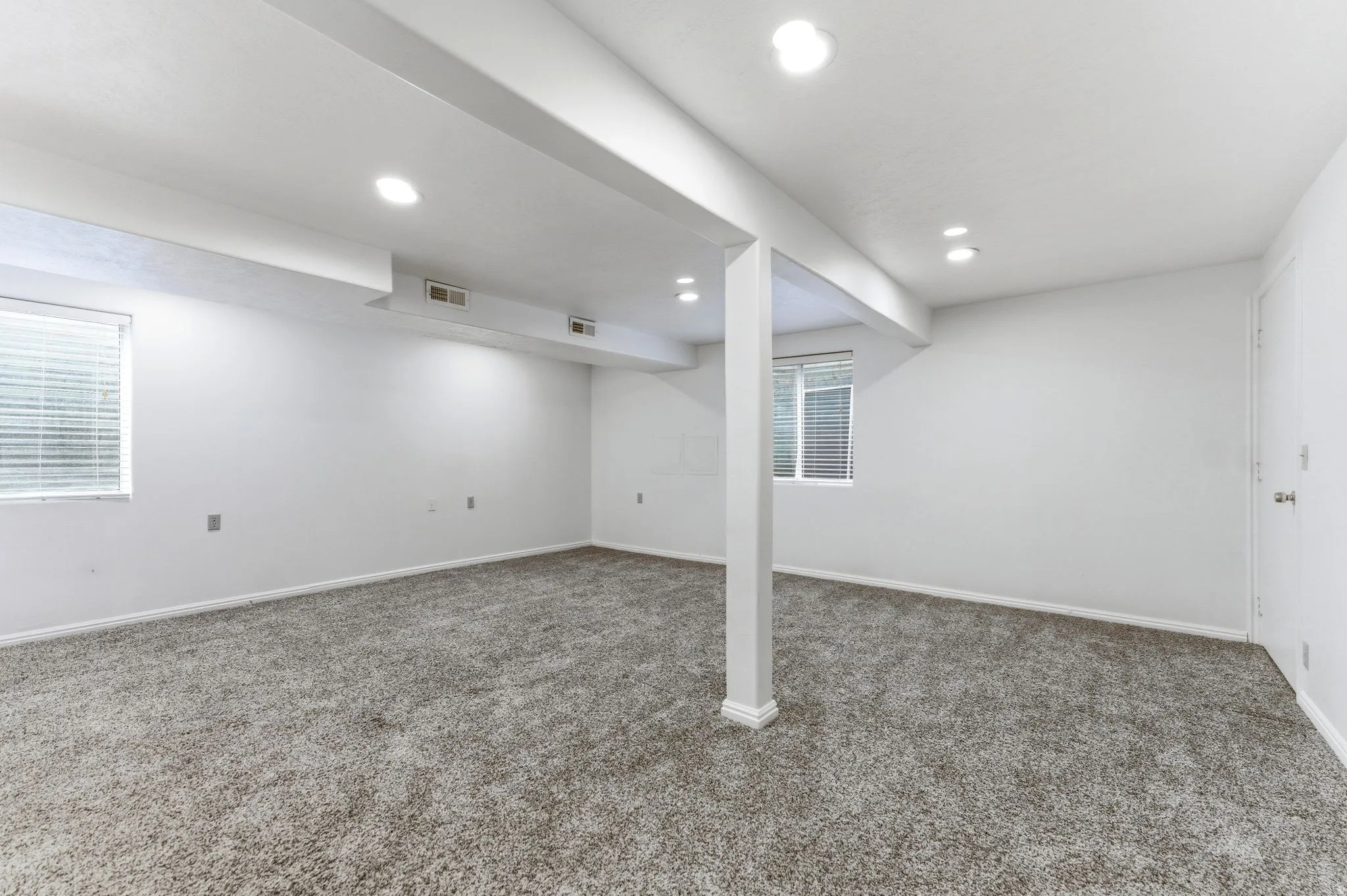 Finished basement space featuring recessed lighting, a neutral carpet, two windows with blinds, and white painted walls