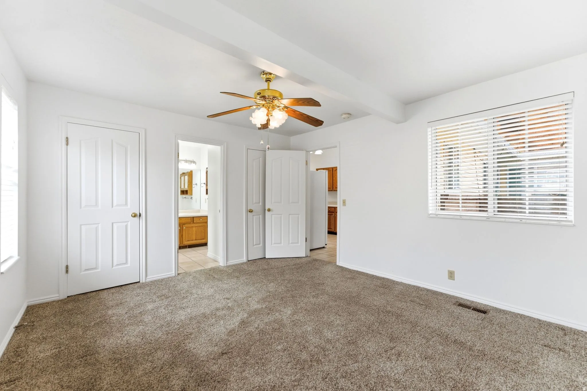Spacious room featuring neutral carpet flooring, white walls, and a ceiling fan with integrated lighting