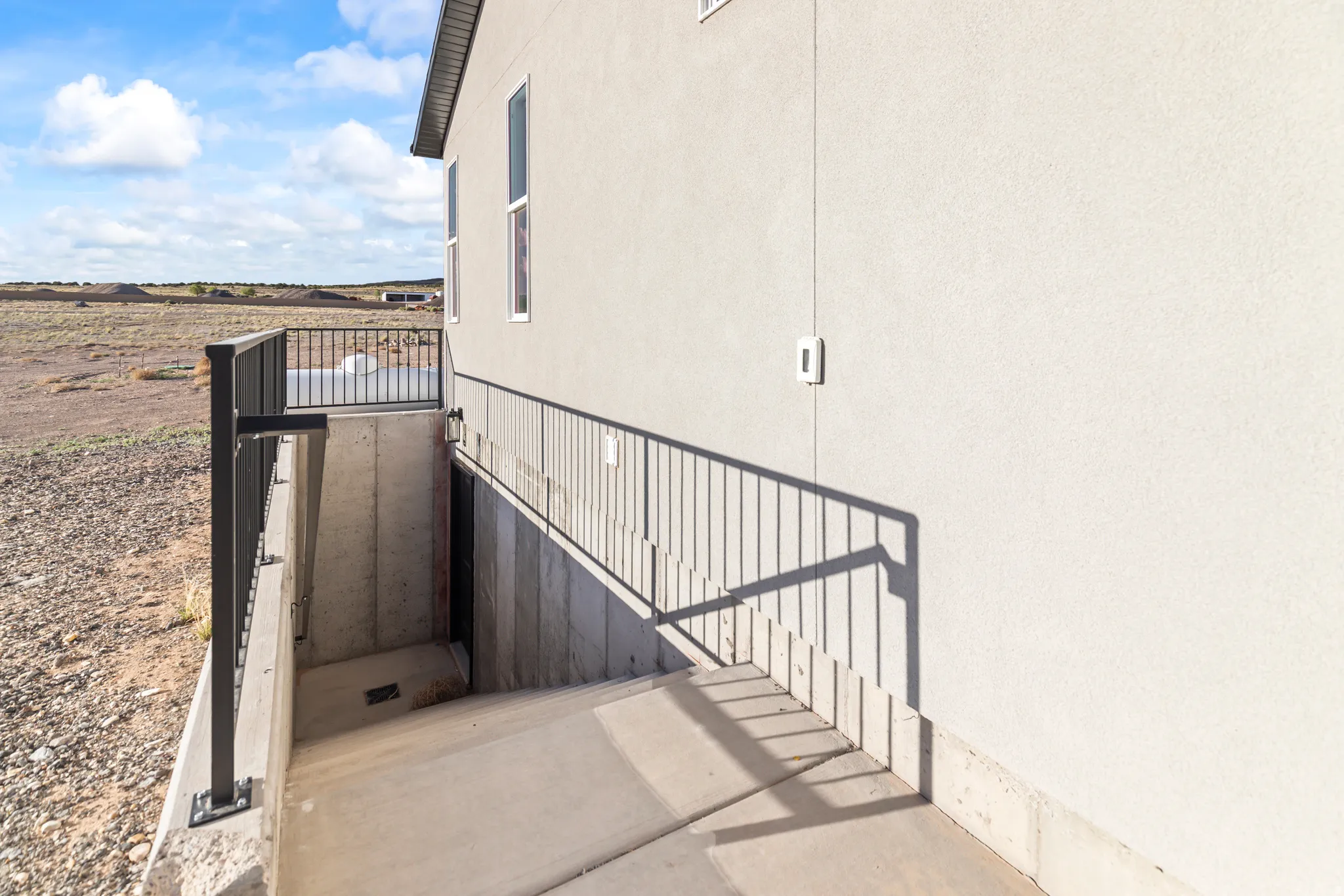 Exterior stucco siding with multiple windows and a black railing system