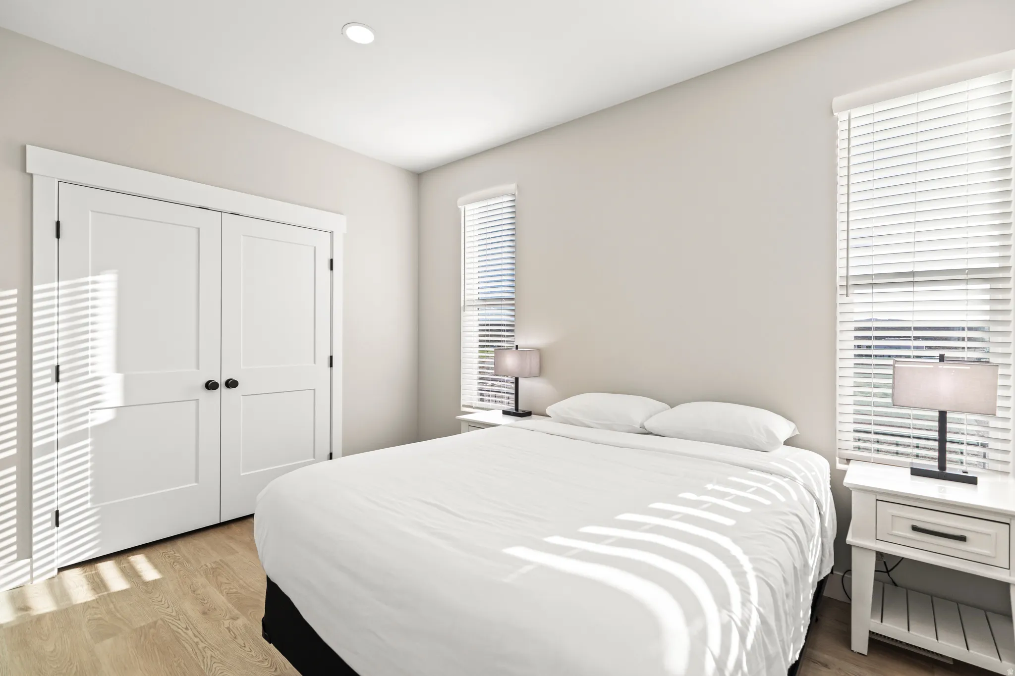 Bedroom featuring wood-finish flooring, dual windows with blinds, recessed ceiling lighting, and a closet with bifold doors