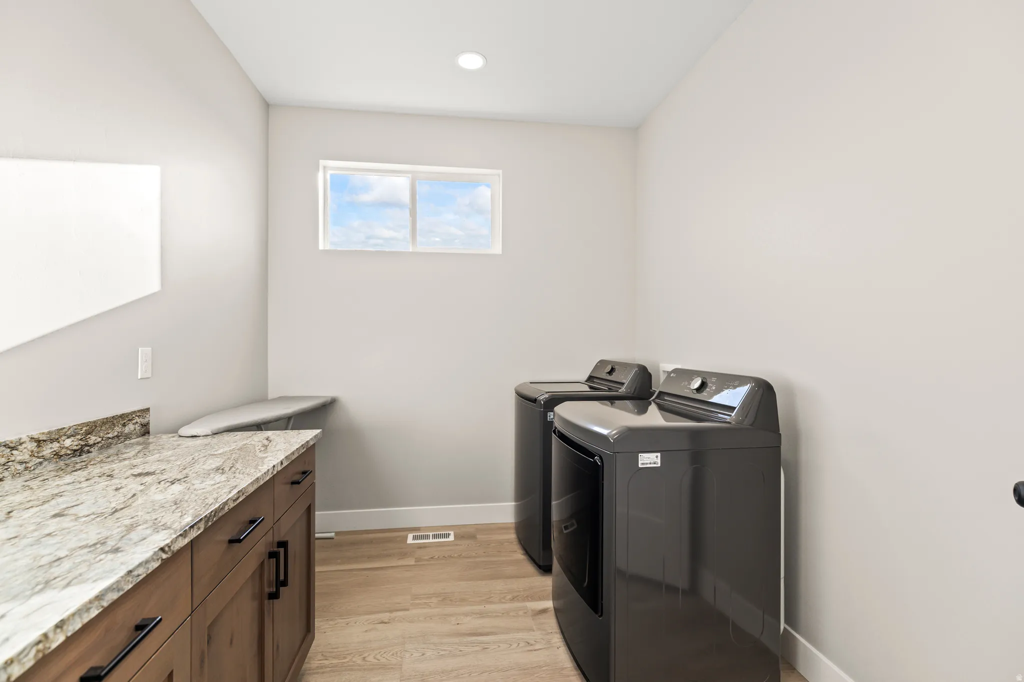 Dedicated laundry room featuring wood-finish flooring, a window providing natural light, and a built-in countertop with wood cabinetry and dark hardware