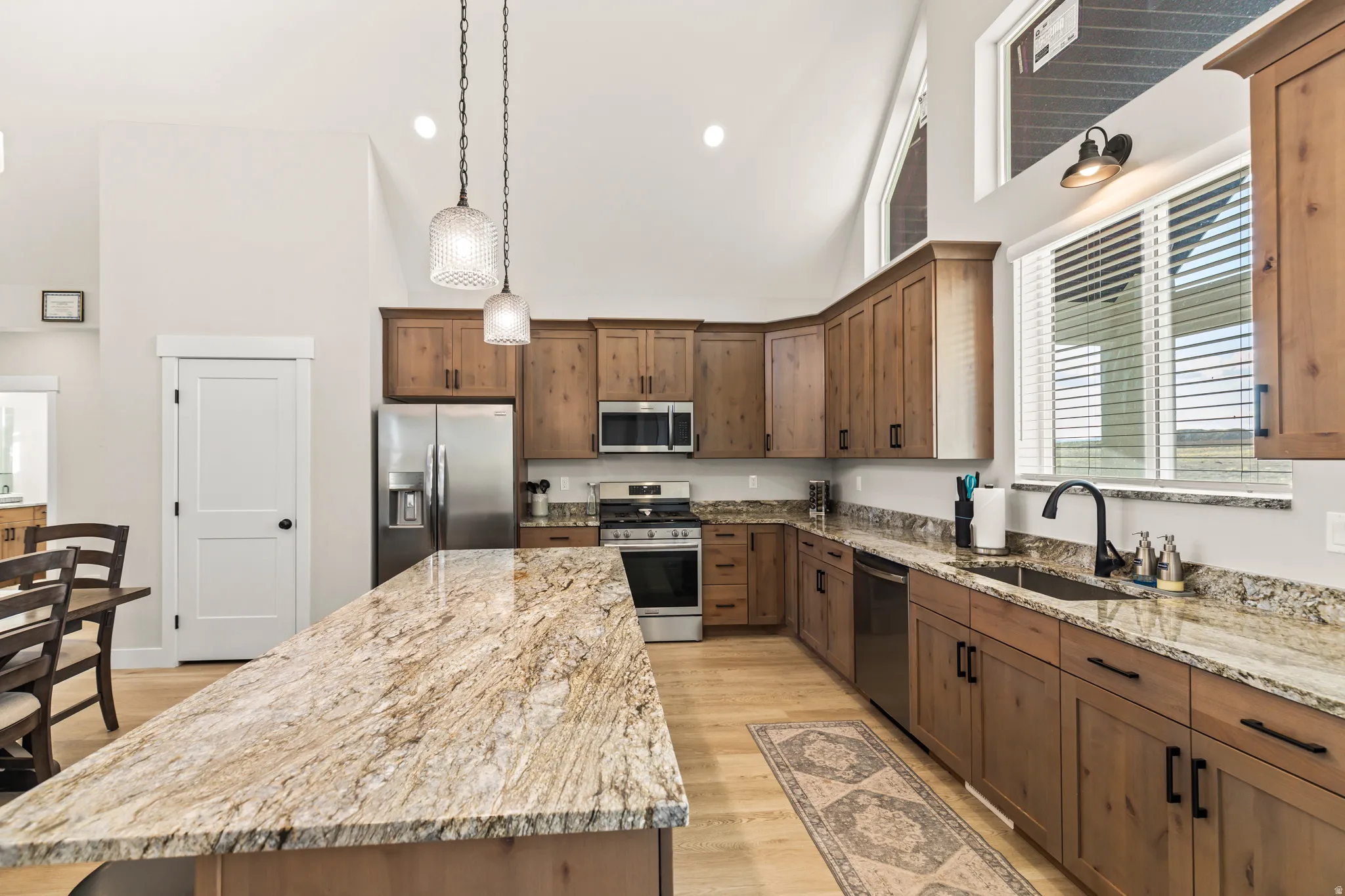 Kitchen featuring vaulted ceilings, wood-finish flooring, light wood cabinetry, a large kitchen island with a stone countertop, and stainless steel appliances