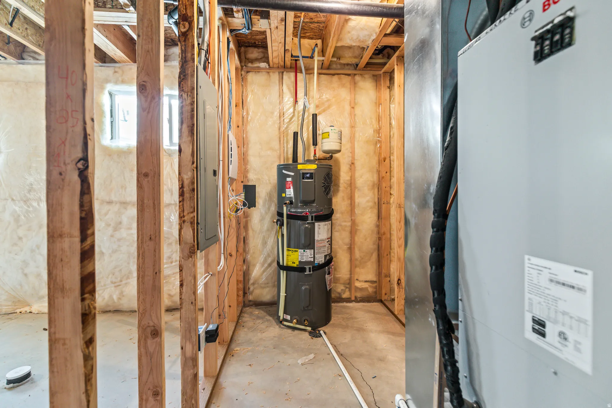 Unfinished basement area featuring exposed wood framing, a visible hot water heater, electrical panel, and HVAC system