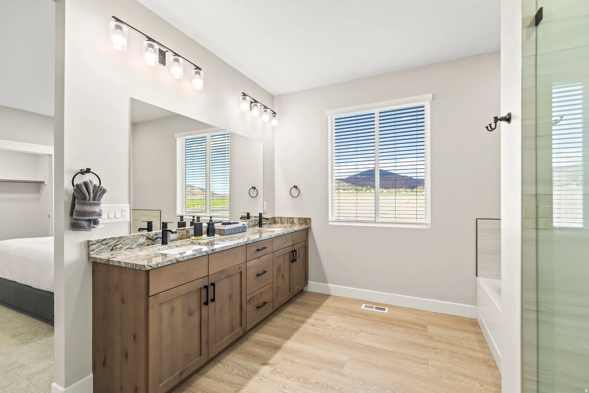 Dual vanity with a stone countertop, light wood-finish cabinetry, and black fixtures