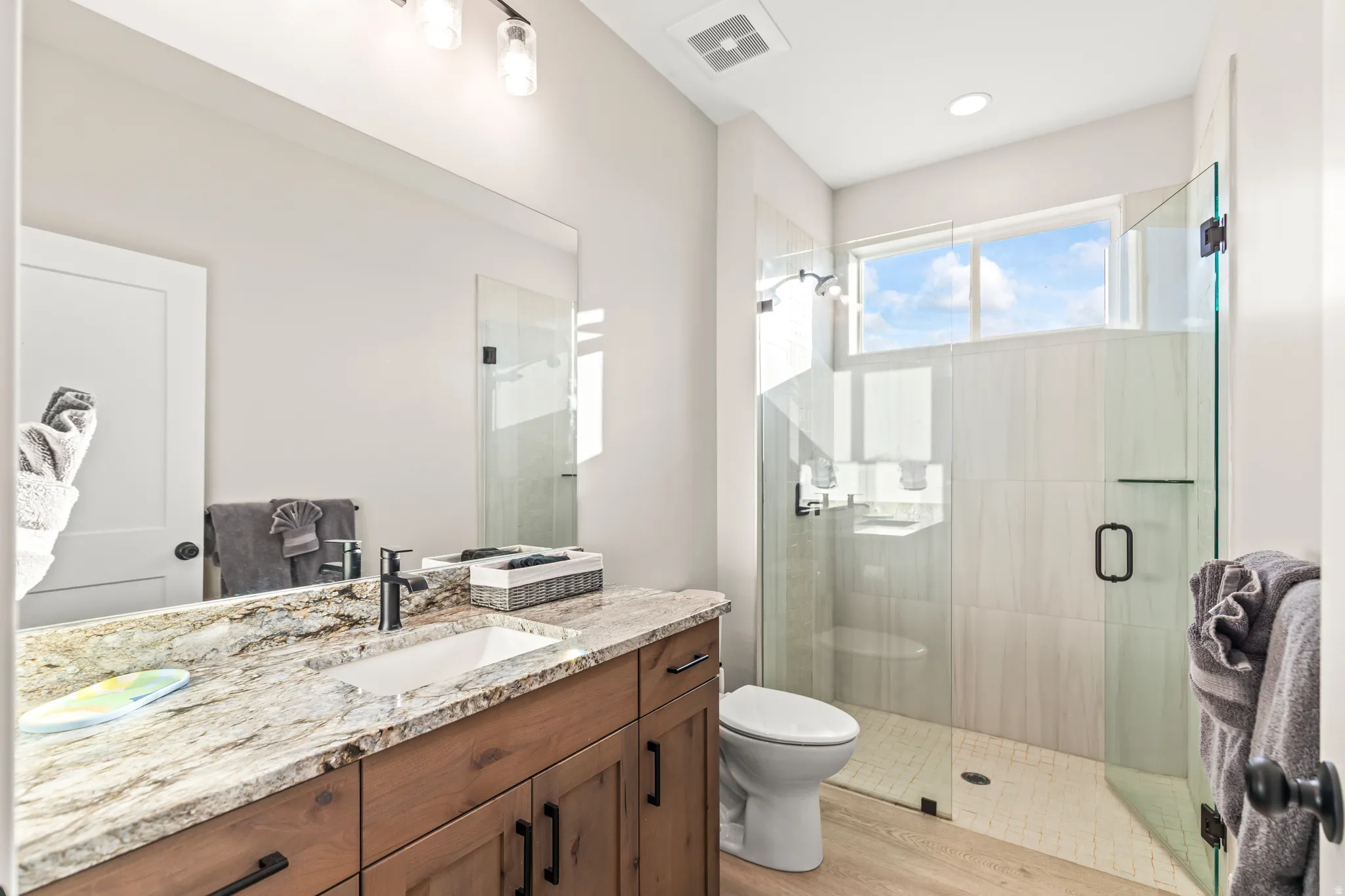 Bathroom featuring a wood-finish vanity with a stone countertop, an undermount sink, and a matte black faucet