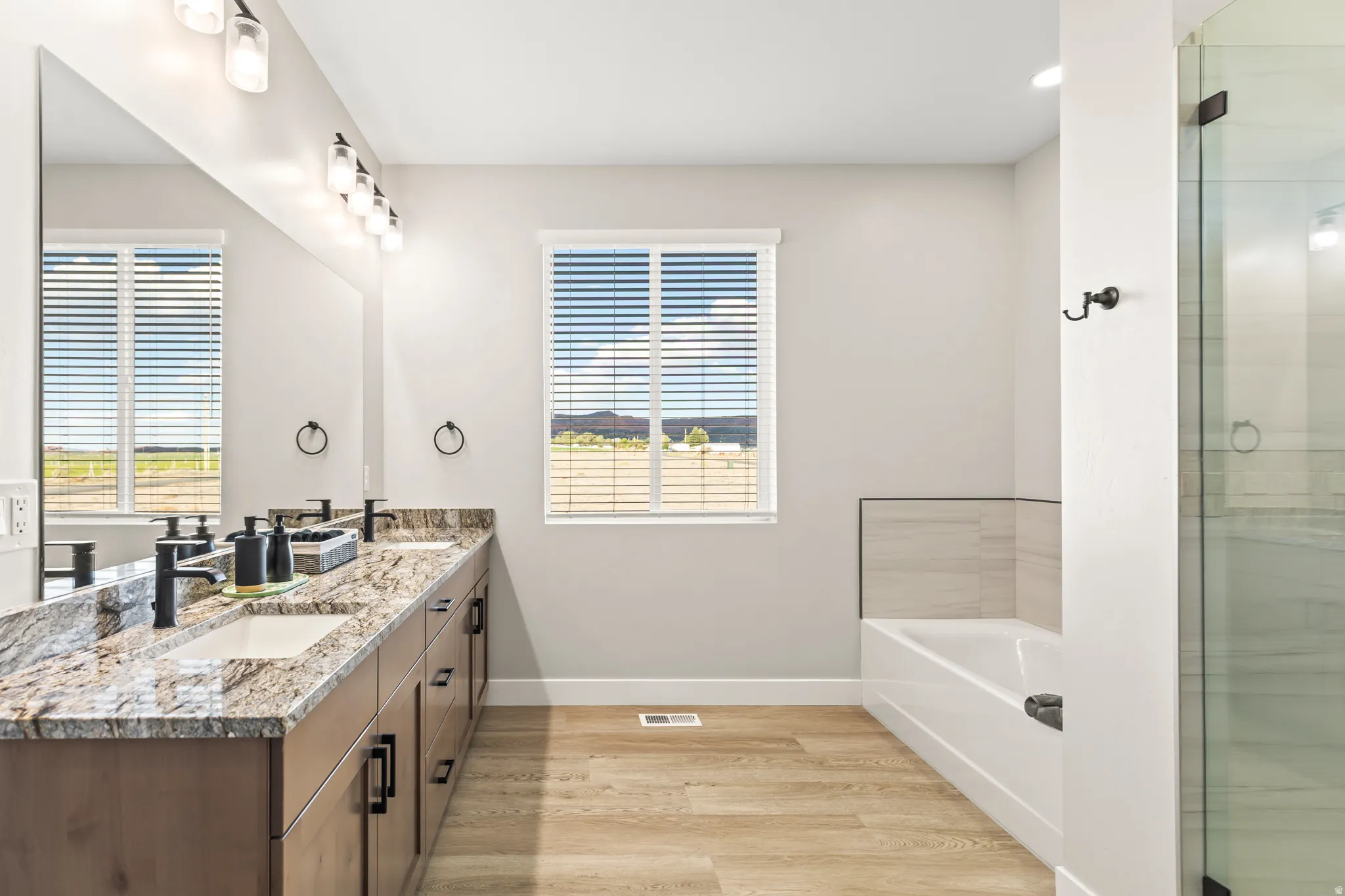 Bathroom featuring a double vanity with stone countertops, wood-finish cabinetry, and matte black fixtures