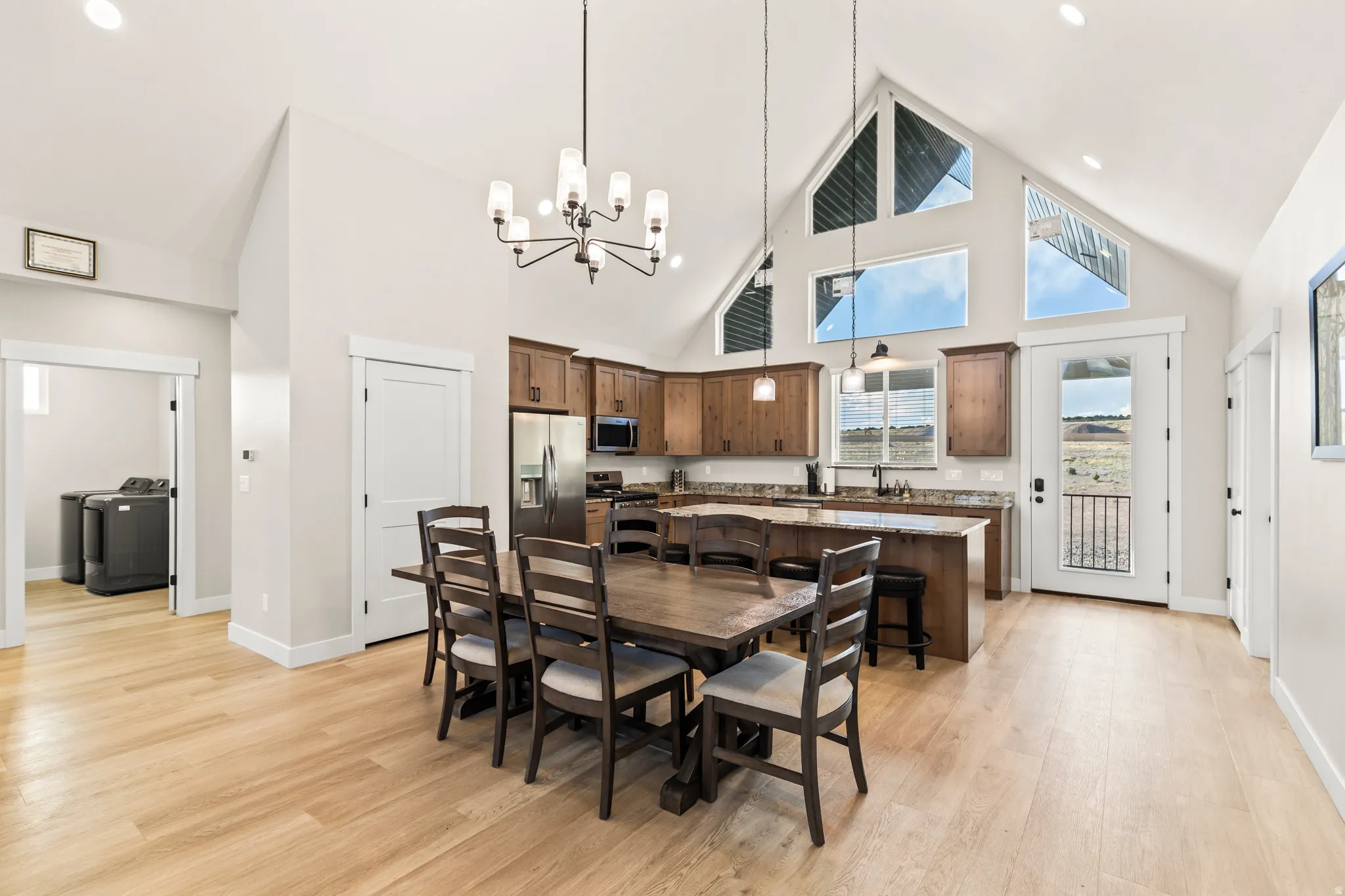 Vaulted ceiling dining area and kitchen featuring natural wood-finish flooring, a contemporary chandelier, and an expansive window arrangement