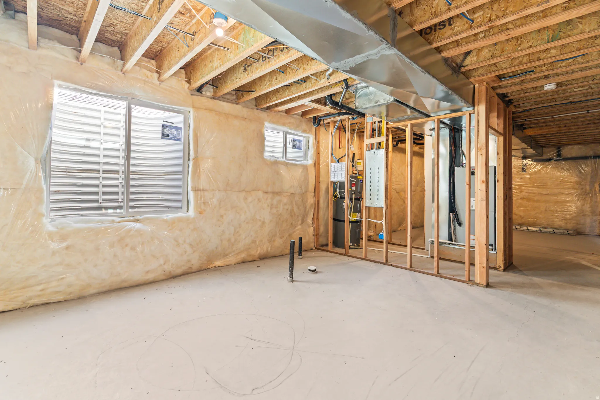 Unfinished basement featuring exposed wood joists, concrete flooring, and multiple window wells