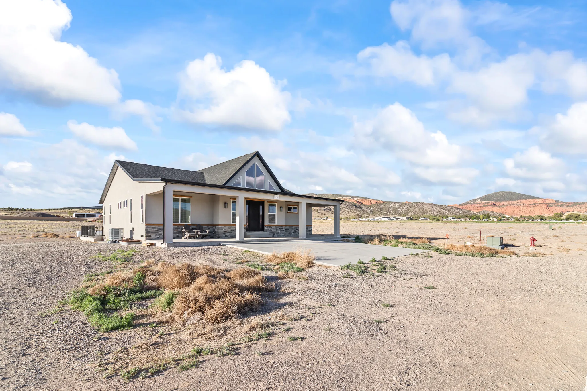 Contemporary-style residence featuring a dark gray shingle roof and a covered porch supported by stone-clad columns