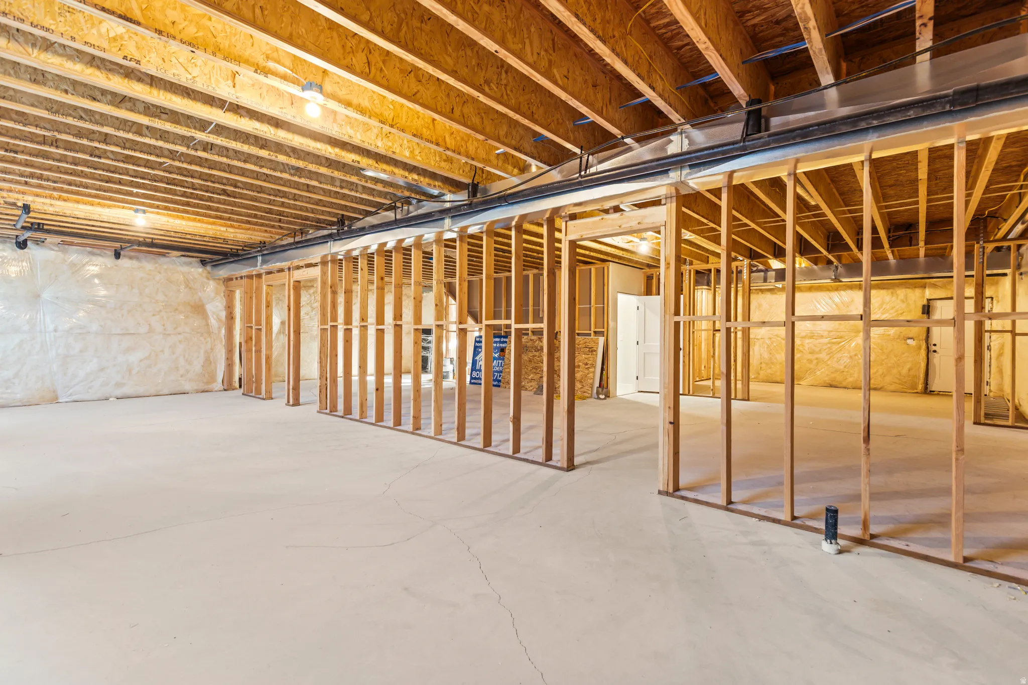 Unfinished basement featuring exposed wood joists, concrete flooring, and roughed-in framing for future rooms