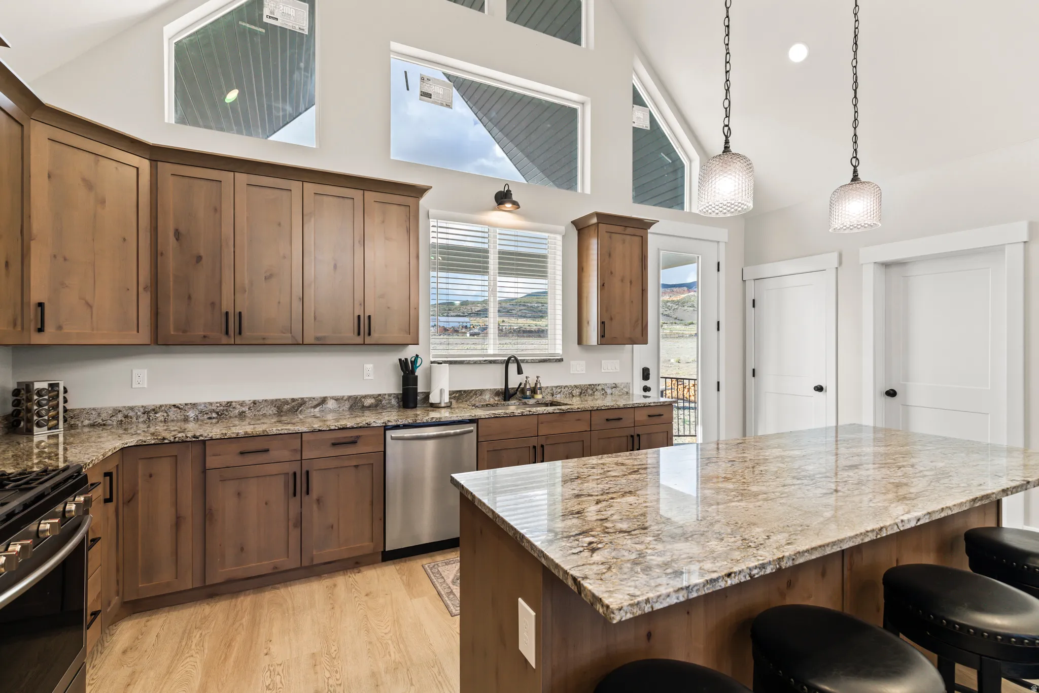 Vaulted ceilings with high windows, wood-finish flooring, stainless steel appliances, wood cabinetry, and granite countertops