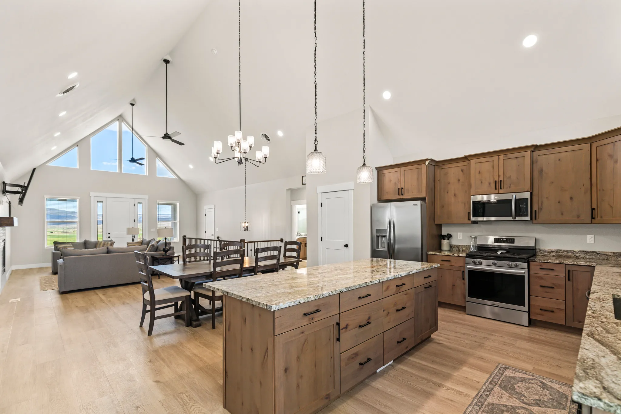 Open-concept living space featuring vaulted ceilings, wood-finish flooring, a kitchen island with stone countertops, stainless steel appliances, and a dining area with a chandelier