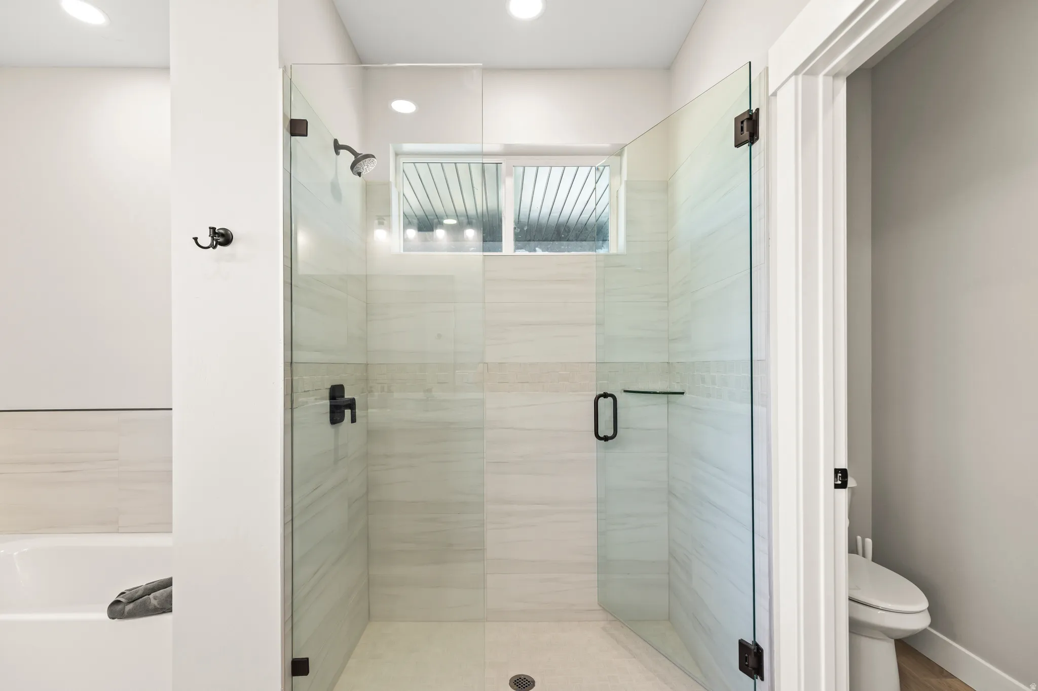 Glass-enclosed shower with matte black hardware, light-toned vertical tile, and a rectangular transom window
