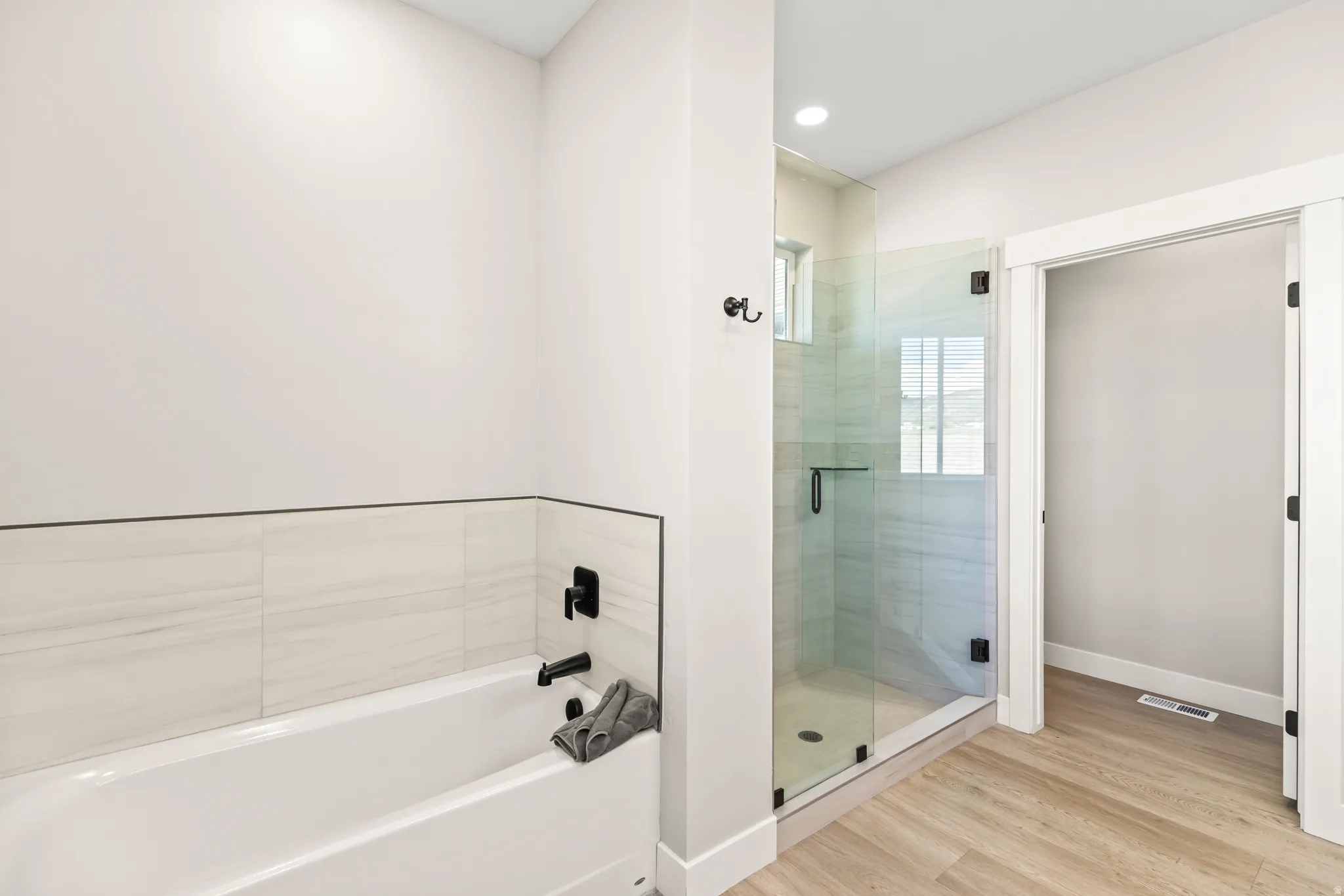 Modern bathroom featuring a glass-enclosed shower with tile surround, a soaking tub with black fixtures, and wood-finish flooring
