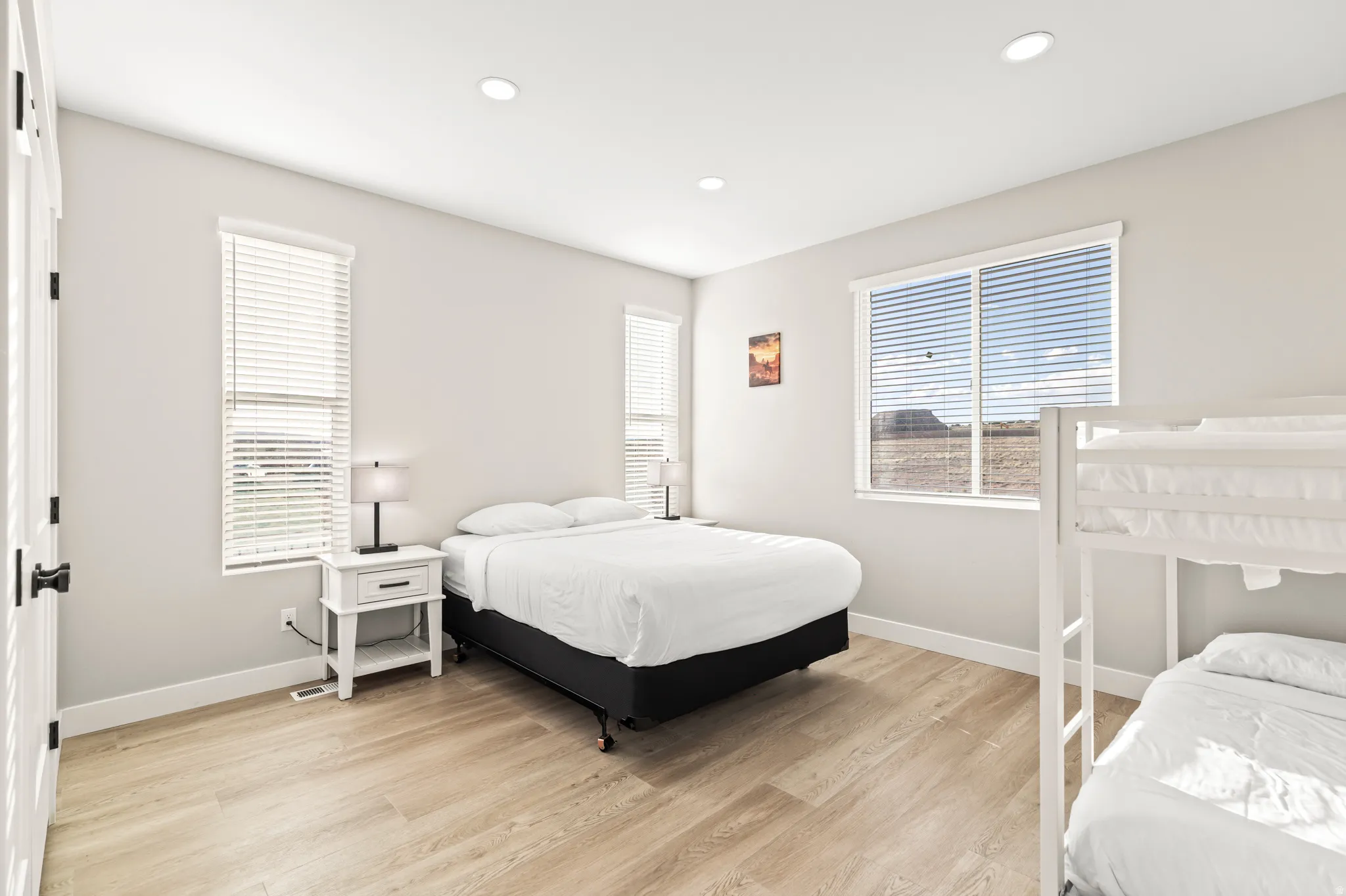 Spacious room featuring light wood-finish flooring and multiple windows with horizontal blinds