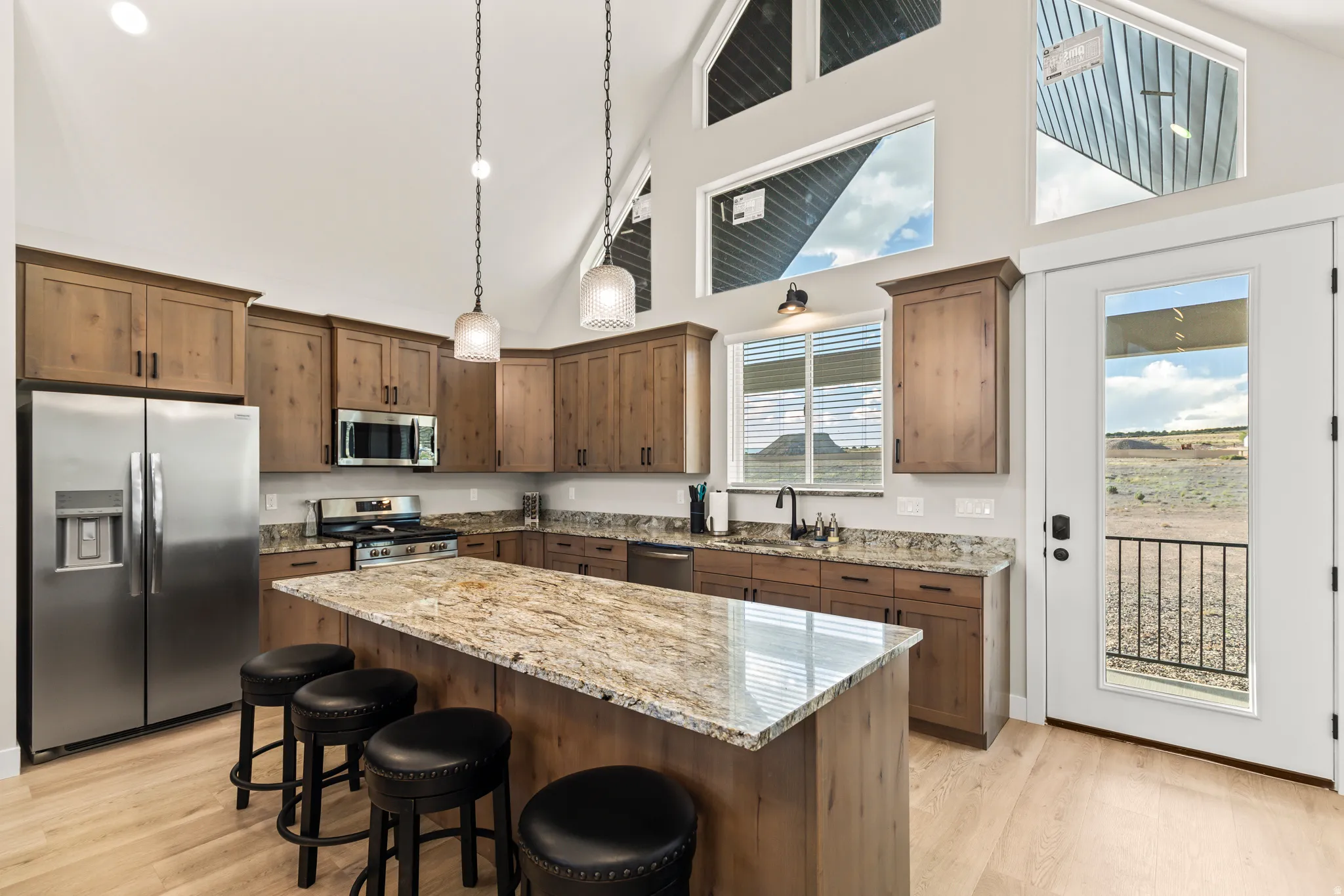 Kitchen featuring vaulted ceilings, light wood-finish flooring, stainless steel appliances, granite countertops, and a full-light exterior door